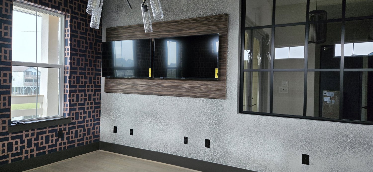 Two wall-mounted TVs set into a wood-paneled recess beside a large black-framed window
