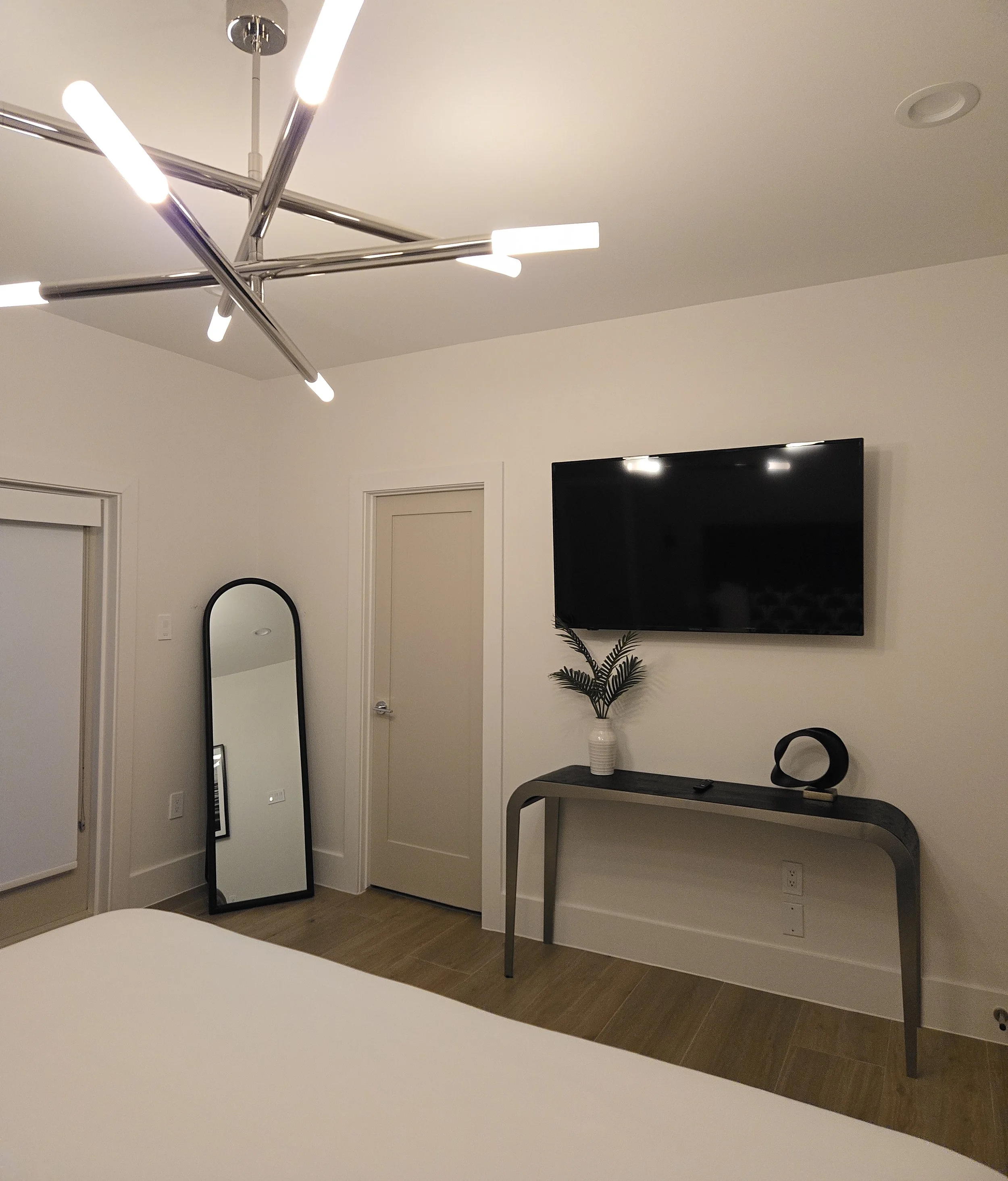 Bedroom with a modern linear chandelier, a wall-mounted TV, and a console table