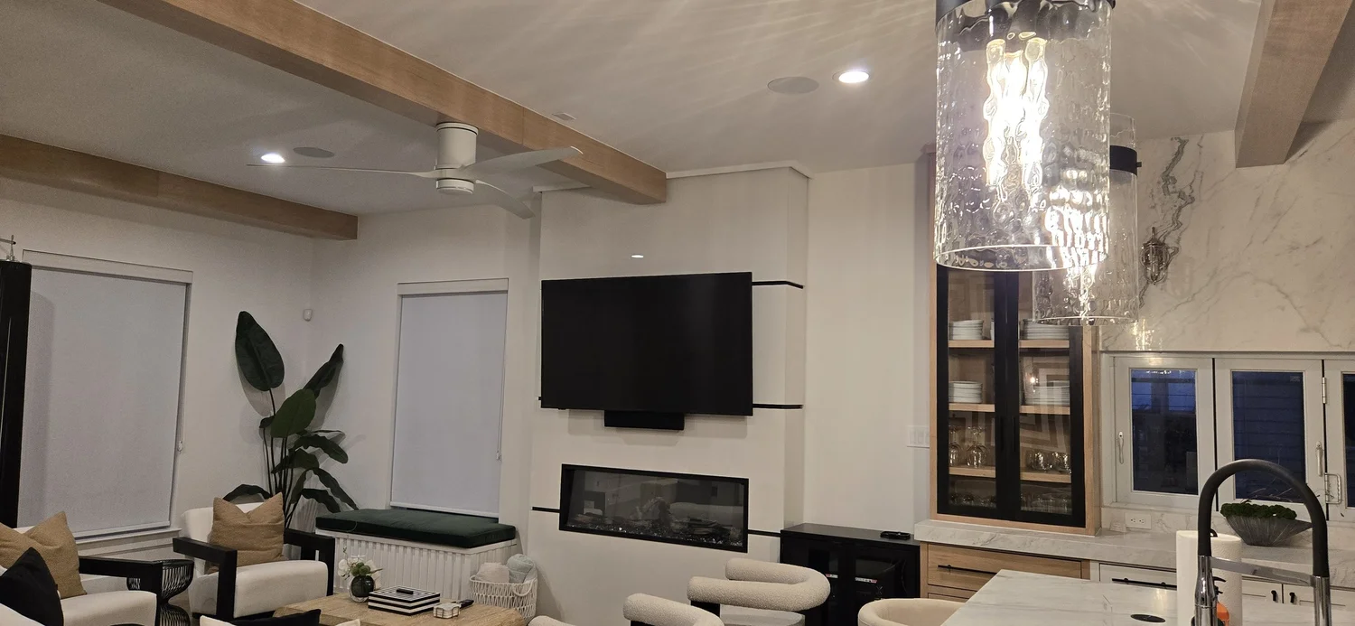 Open living room with a wall-mounted TV above a linear fireplace, white walls and wood ceiling beams