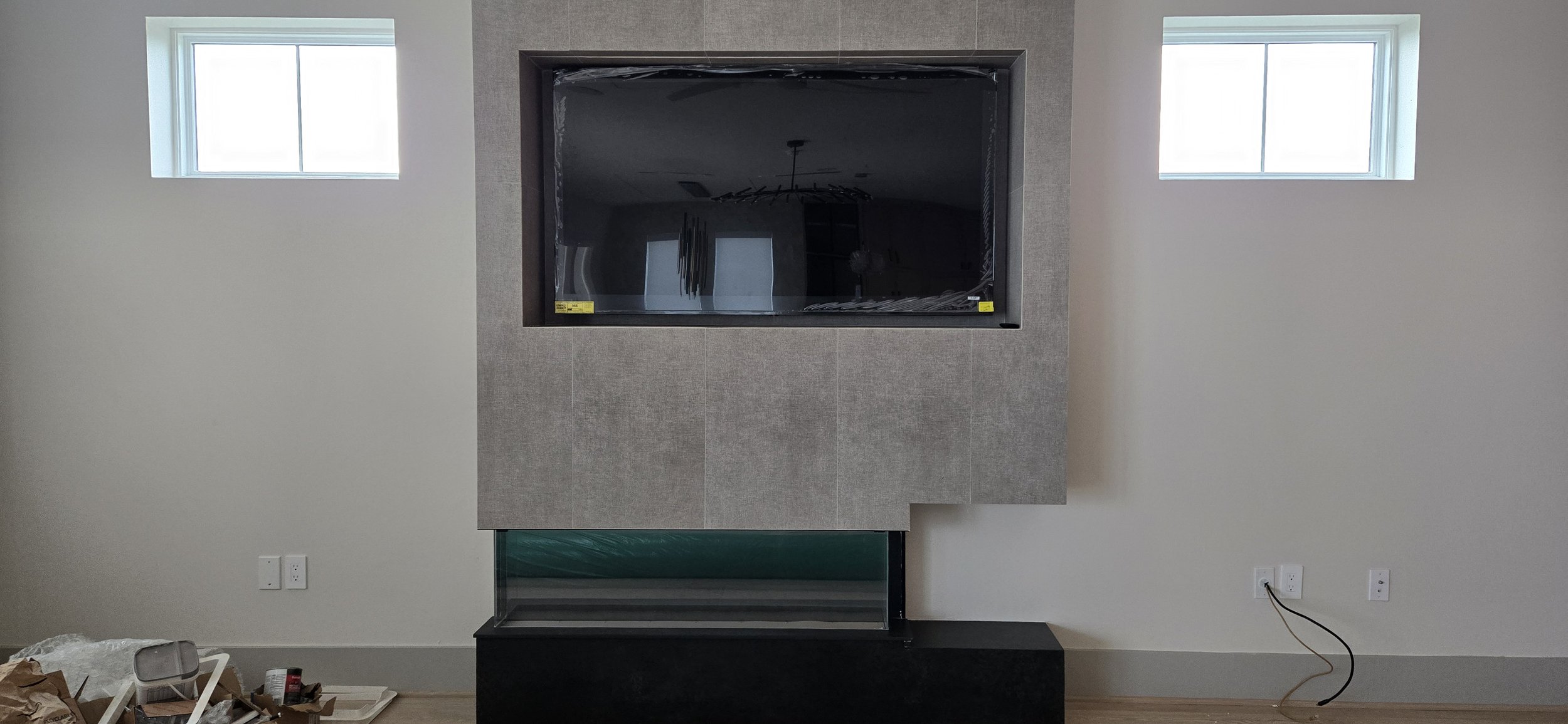 TV mounted in a recessed stone-textured fireplace surround with wiring outlets below, during construction