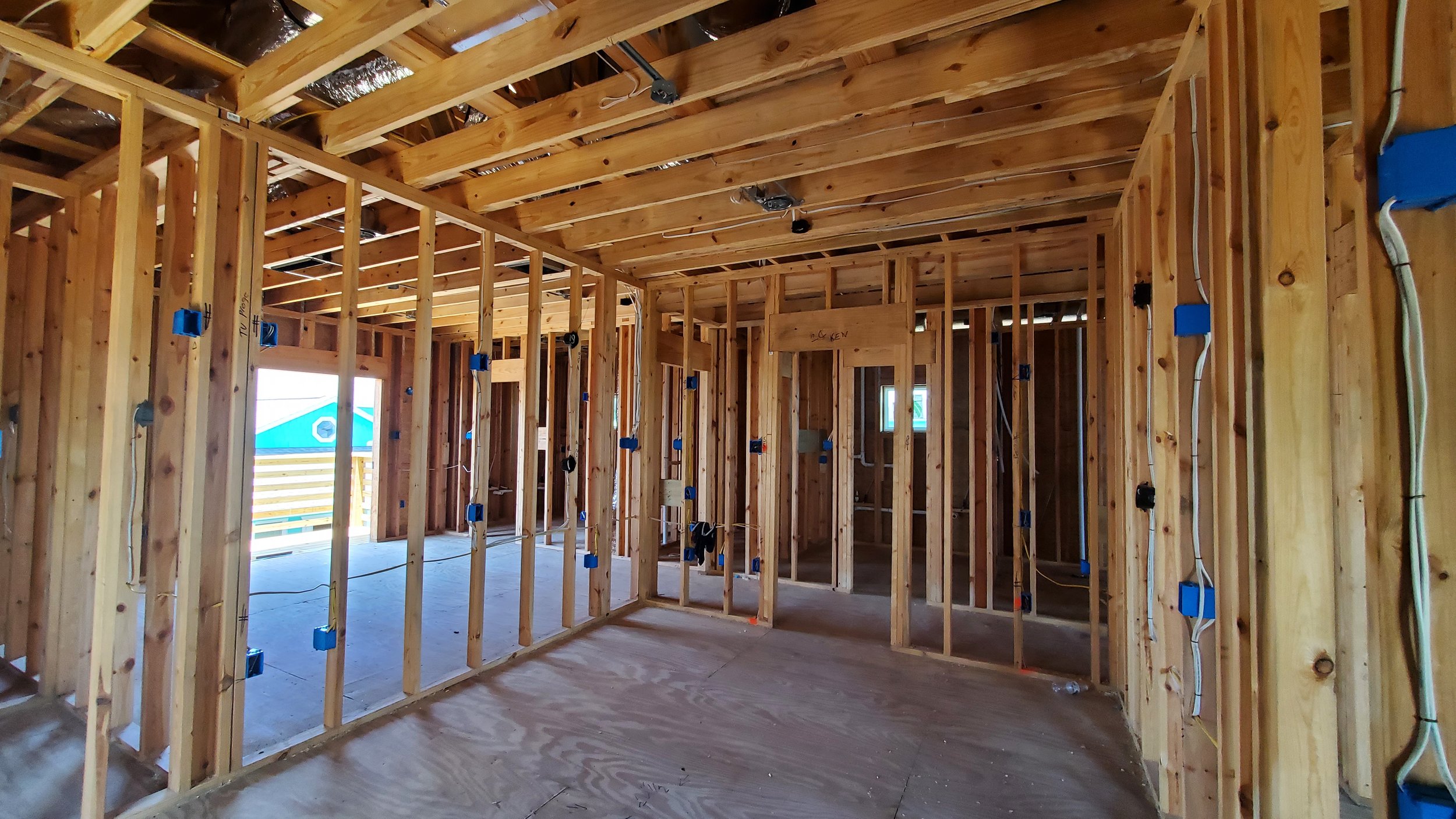 Open wall framing and ceiling joists with blue electrical boxes and rough-in wiring before drywall