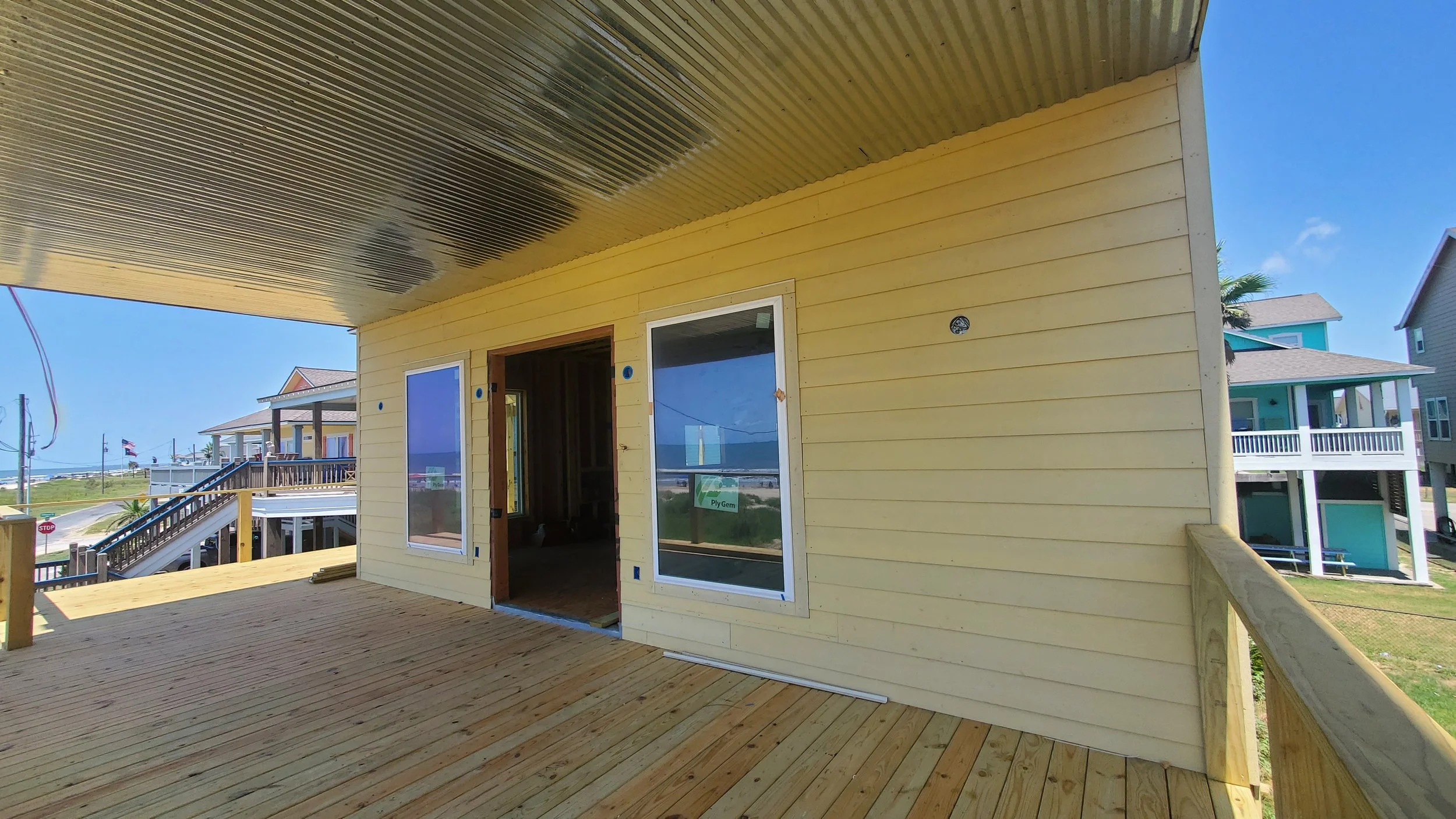 Back of a new yellow siding house at framing stage, with an unfinished wood deck and bay-view windows