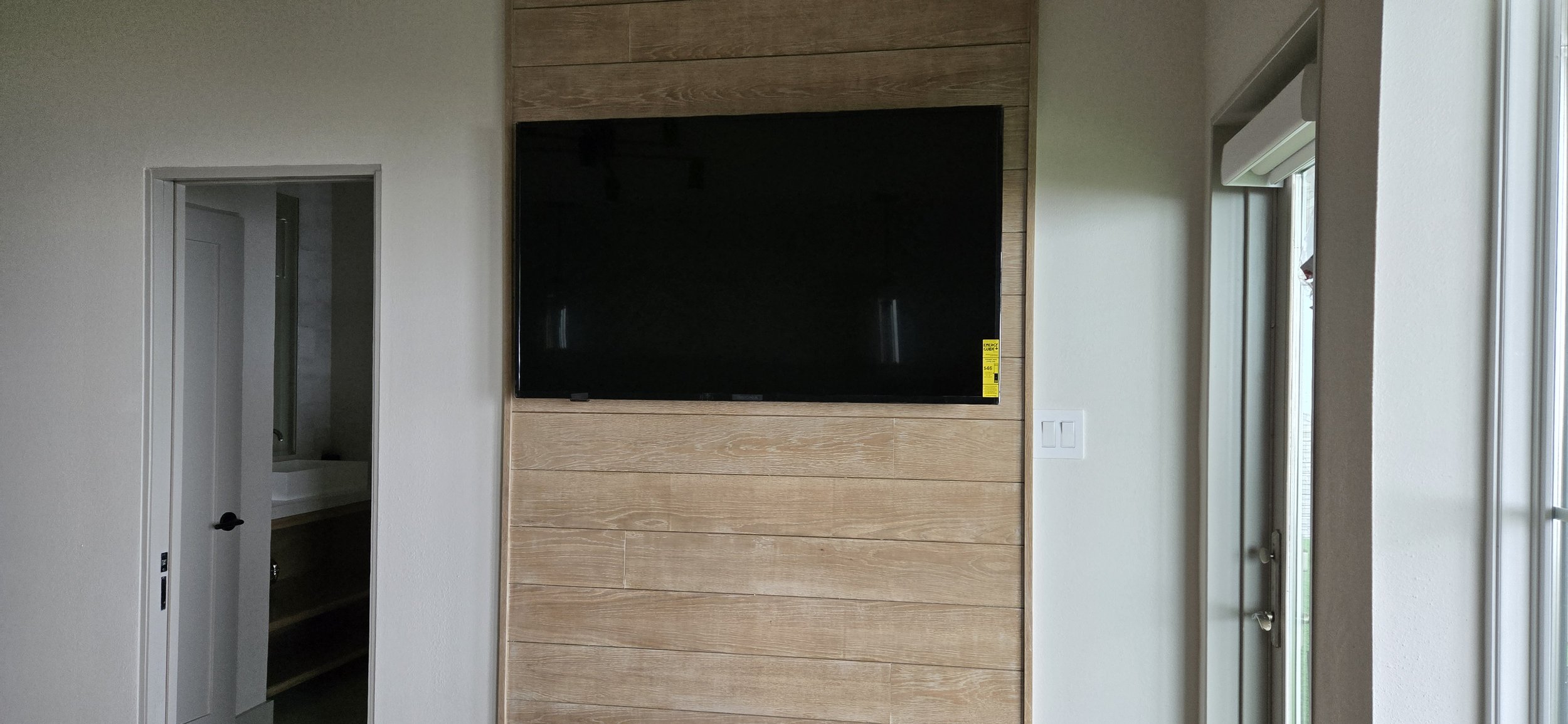 Wall-mounted TV on a wood-plank feature wall between a doorway and a window, during construction