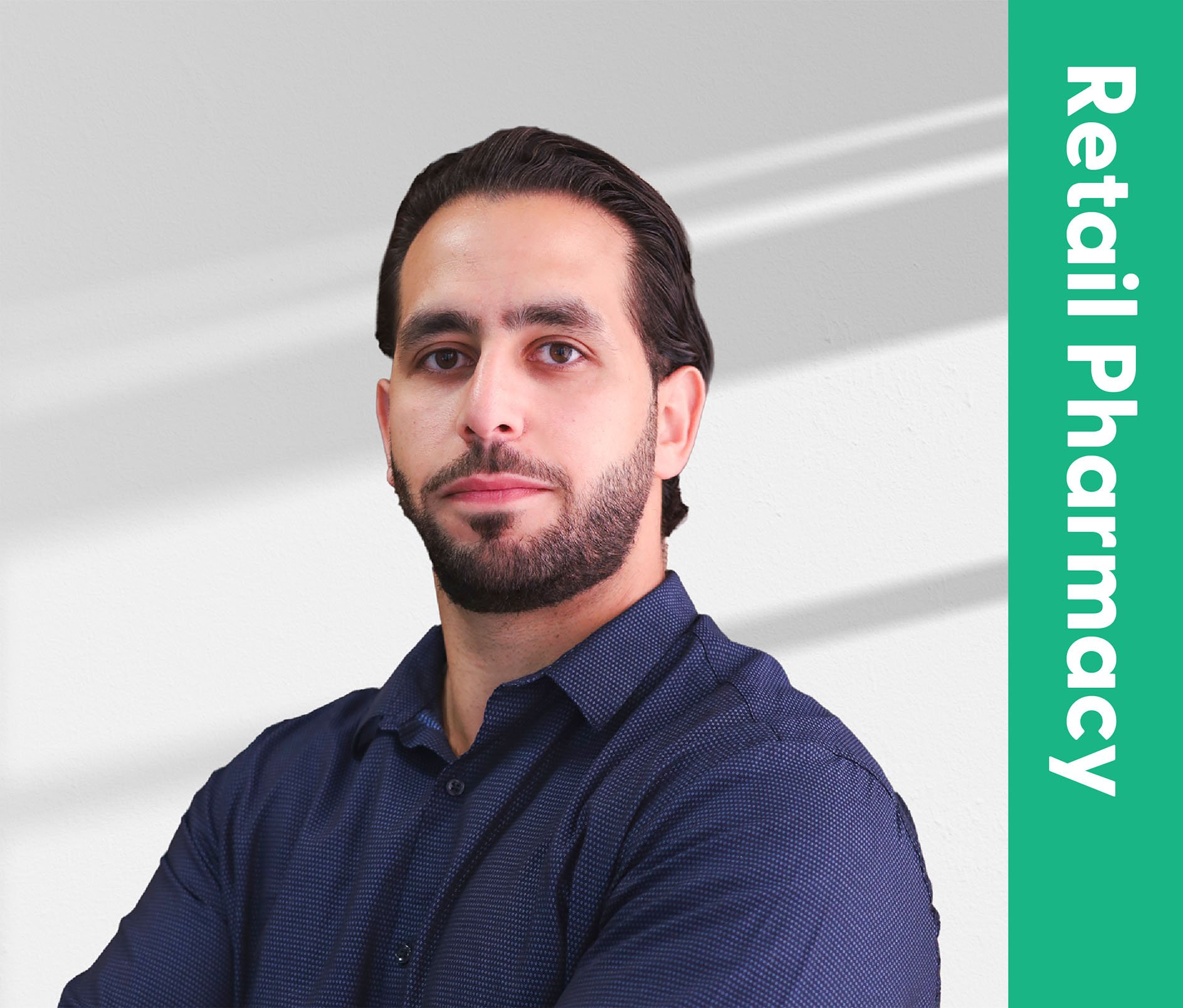 Close-up of a man with dark hair and a beard, wearing a dark blue patterned shirt, standing against a plain light gray background. Green vertical banner on the right reads 'Retaliation Pharangy'.