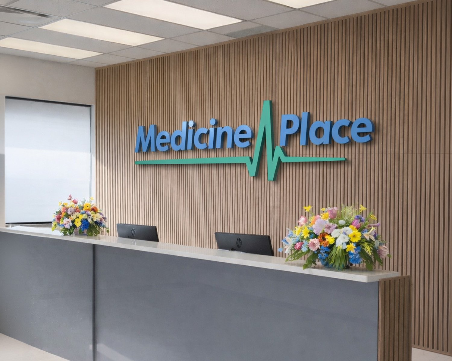 Reception area at Medicine Place with a wooden wall, a sign with a heart rate line, two computer monitors, and two flower arrangements on the counter.
