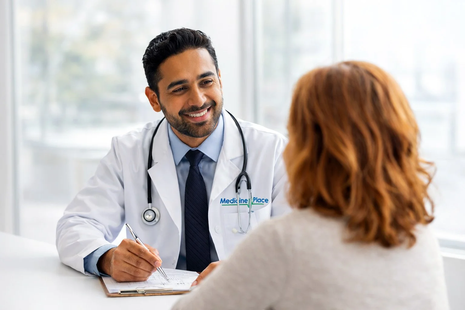 A male doctor with a stethoscope around his neck smiling during a consultation with a female patient in a medical office.