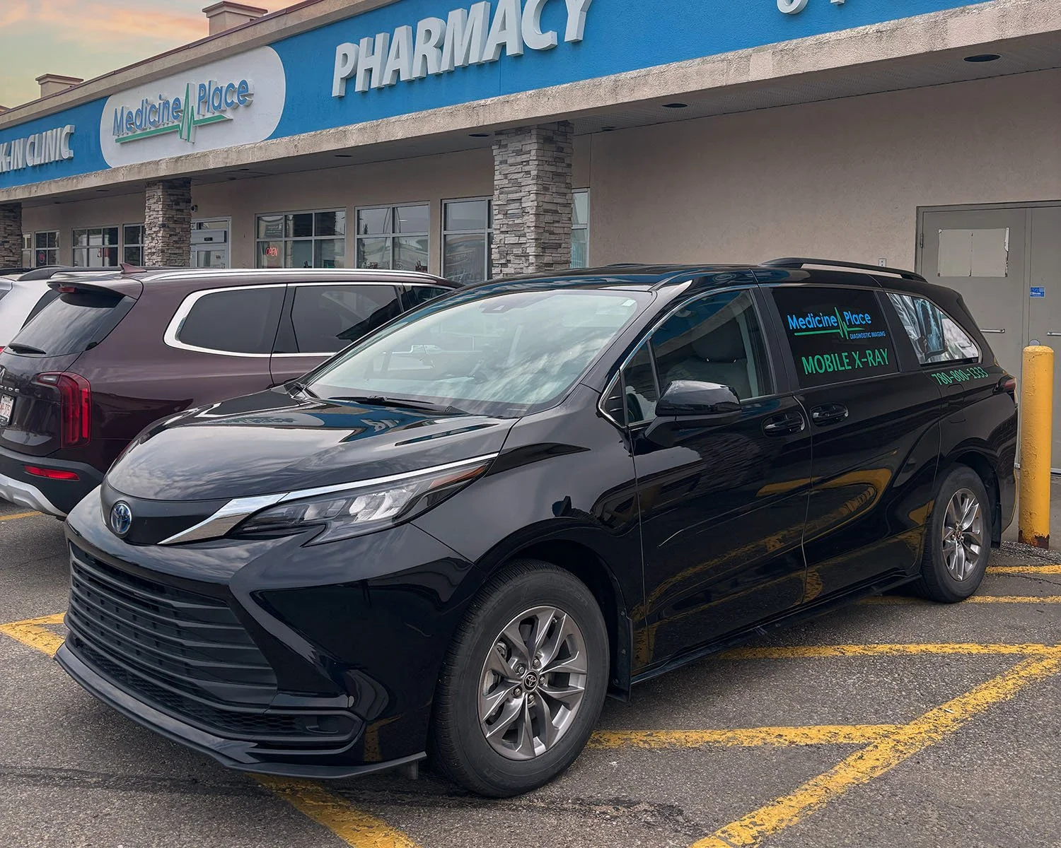Black Toyota Sienna minivan parked in front of a pharmacy with the sign 'Medicine Place' visible above. The van has signage on the side advertising mobile X-ray services, showing the name 'Medicine Place' and a phone number.