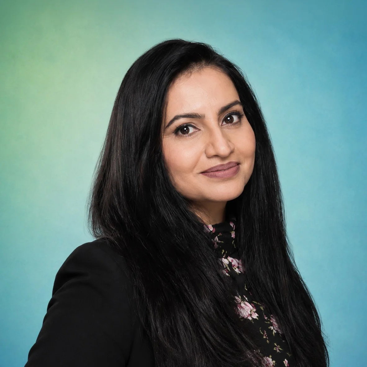 Portrait of a woman with long black hair, wearing a black jacket over a floral top, against a colorful background.