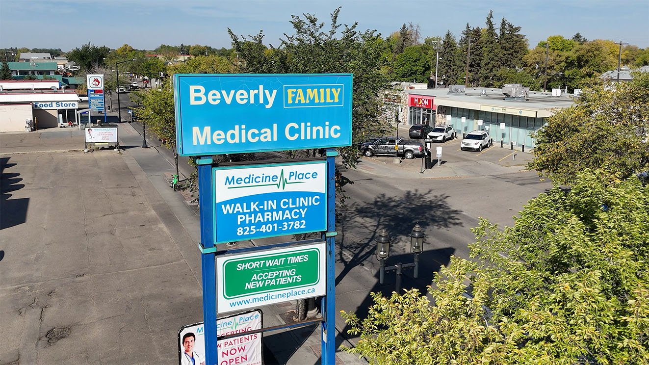 Sign for Beverly Family Medical Clinic with other signs indicating walk-in clinic, pharmacy, and short wait times accepting new patients, located in a commercial area with parking lot and trees.