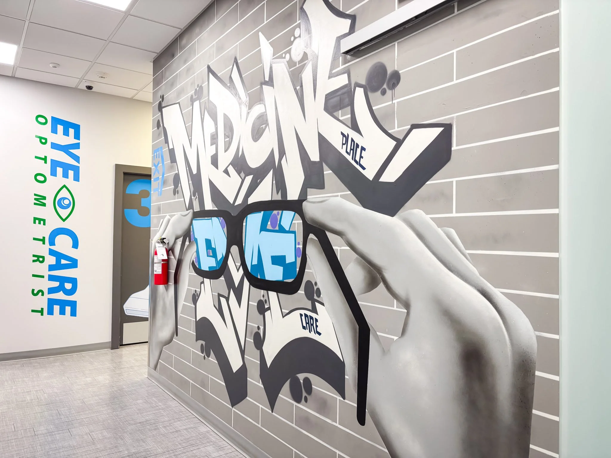 Wall mural depicting a hand holding sunglasses with the word medCare graffiti-style text, and a sign for eye care with an eye icon on an adjacent wall.