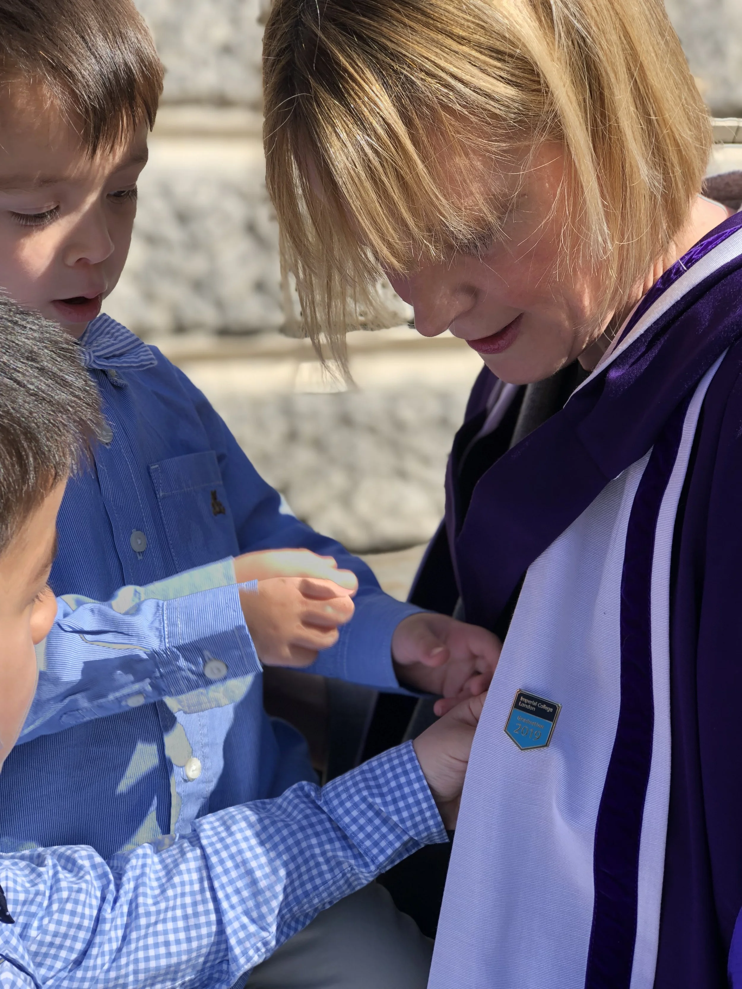 Dr Janet Deane with her young children, interested in her PhD graduation gown and badge to represent the PhD mum journey