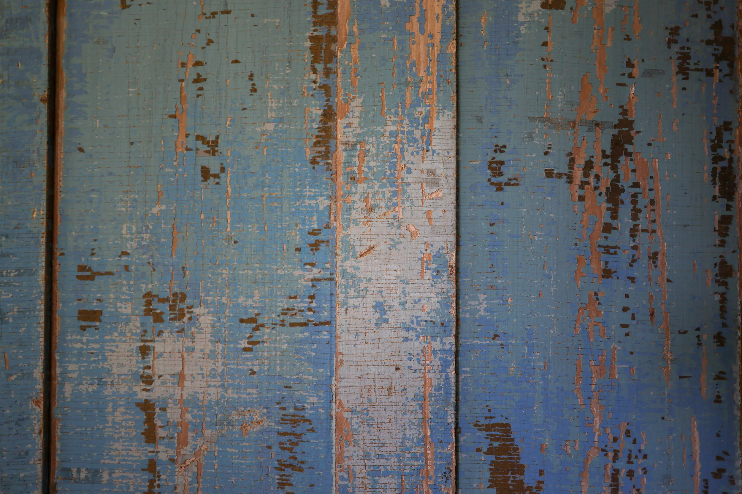 Close-up of weathered wooden planks painted blue, with chipping and peeling paint revealing the wood underneath.