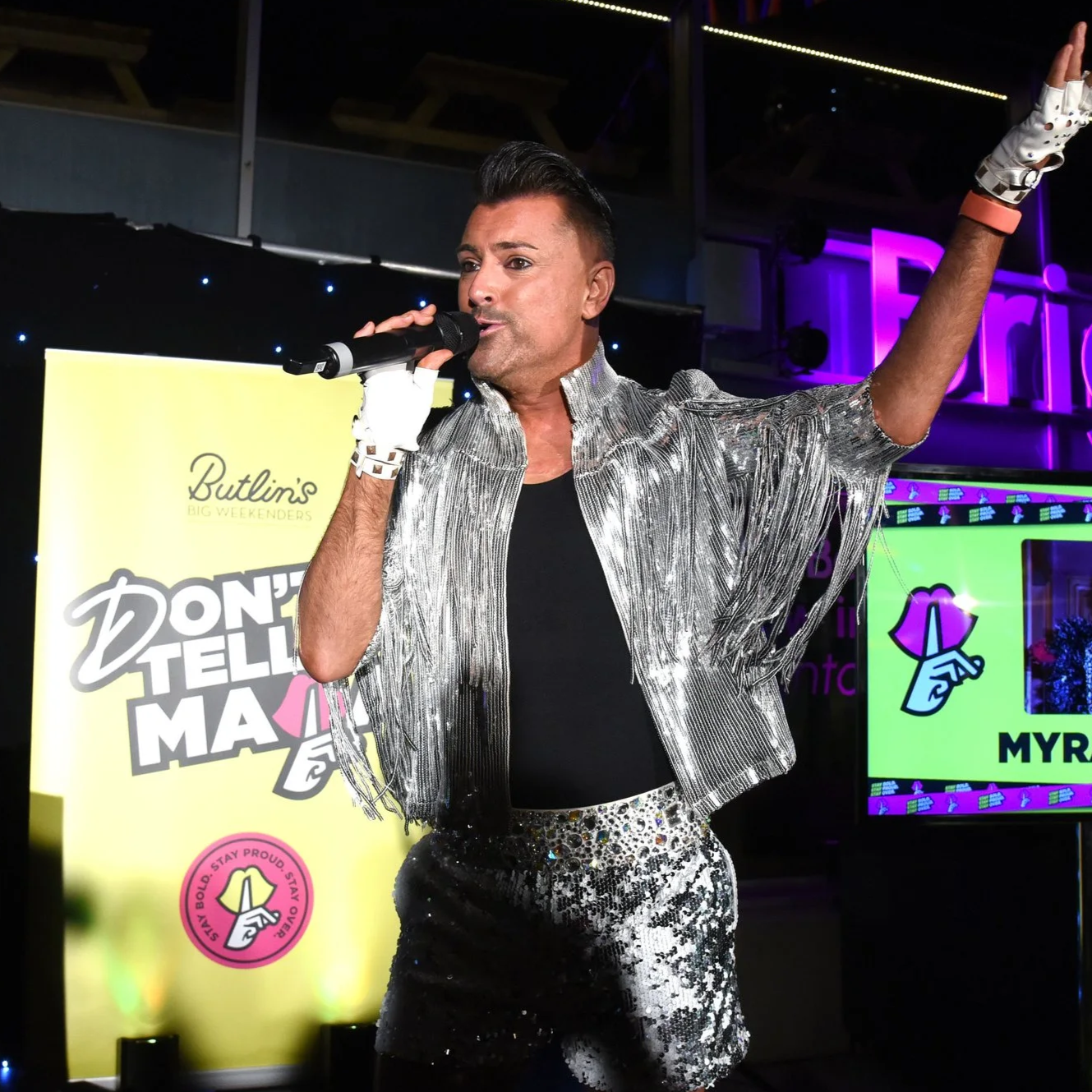 Three men posing shirtless in swimwear by a pool, with scenic mountains and trees in the background.