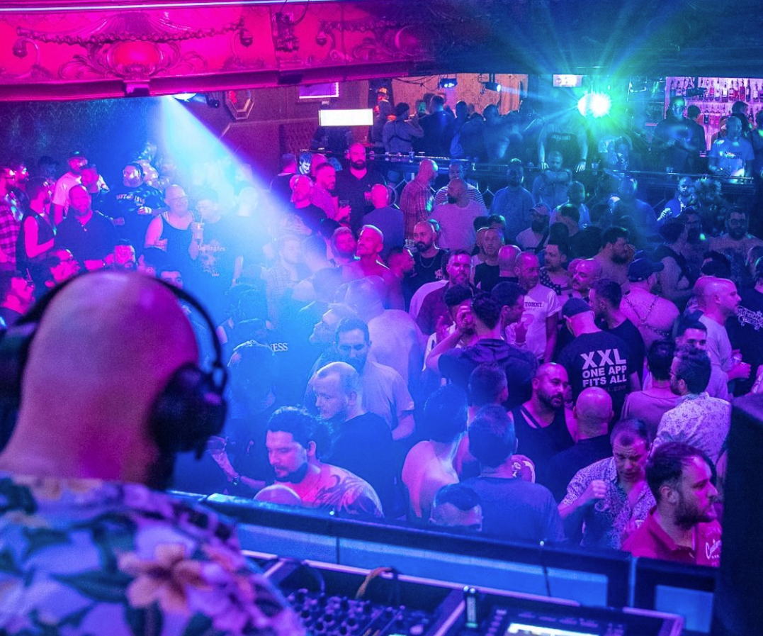 a club night with a DJ on the deck and a busy crowd under blue and pink lighting