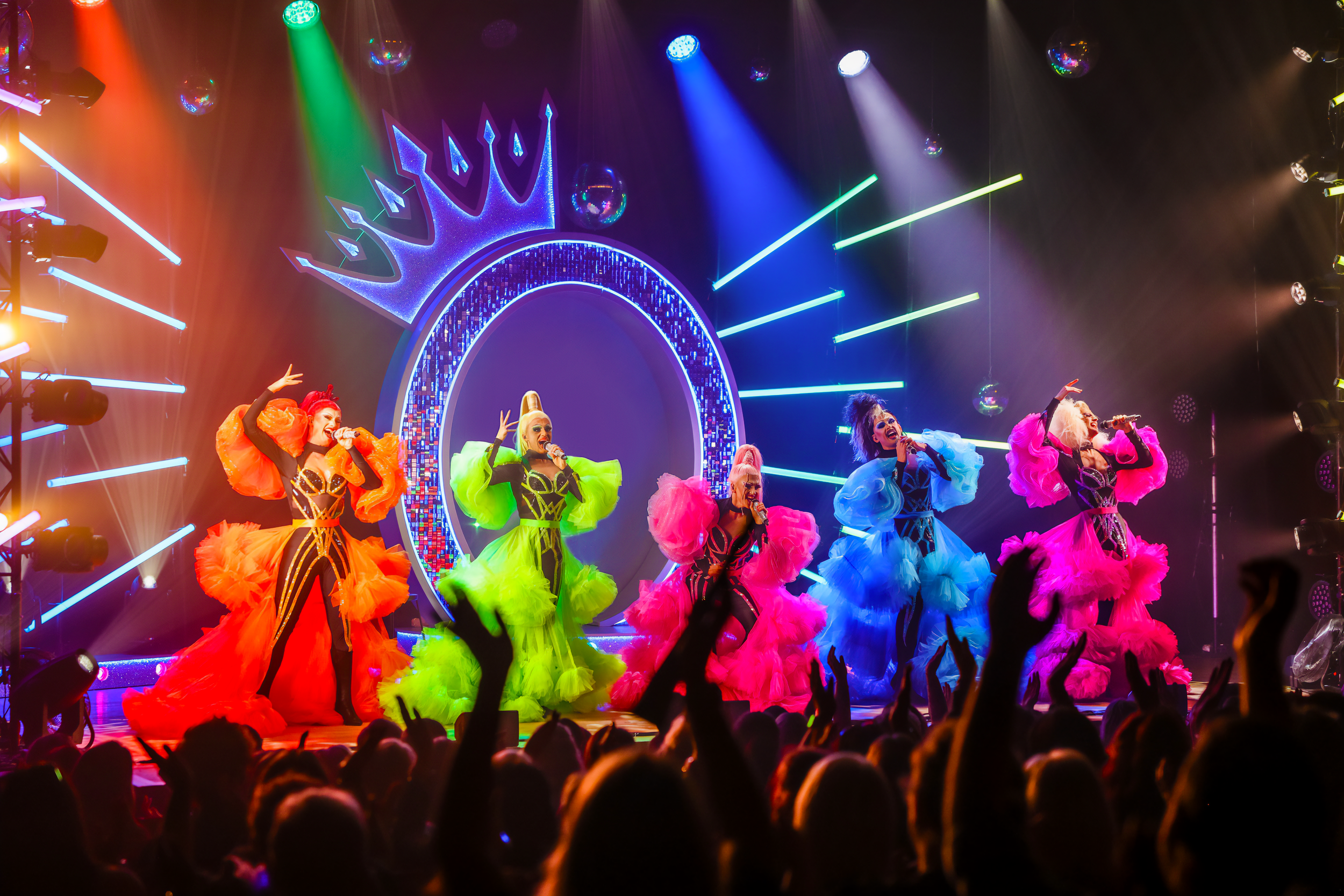 five performers on stage in colourful neon outfits performing to a crowd