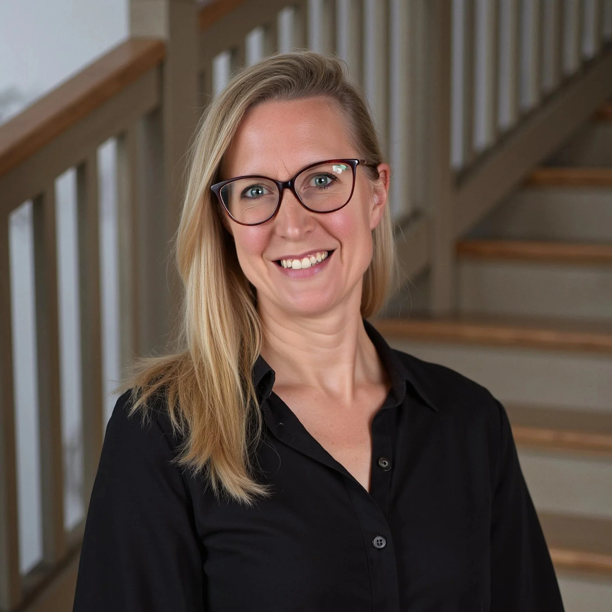 Das Bild zeigt ein Profilbild von mir in schwarzer Bluse und dunkler Brille. Offene blonde Haare und ein offenes Lachen laden Dich auf meine Seite ein.