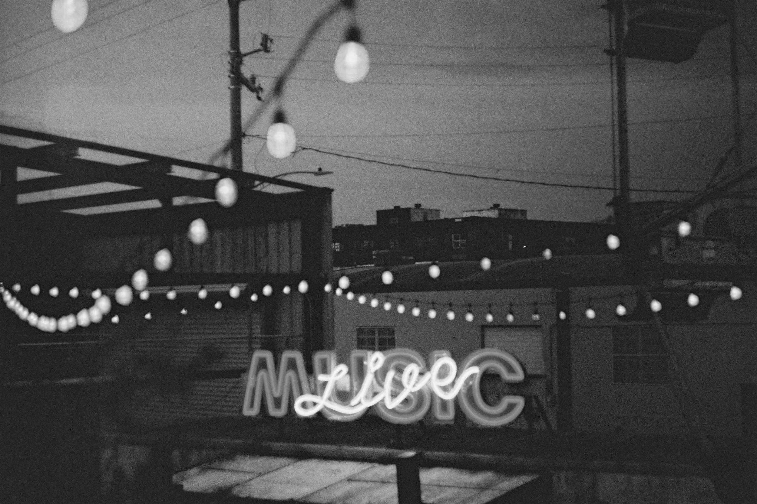 Black-and-white exterior of an independent live music venue with string lights and neon signage