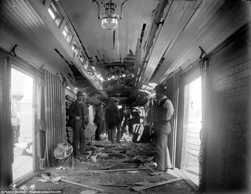 Interior of a building with significant damage, debris on the floor, and several men inspecting the scene. The ceiling is extensively damaged, with hanging and collapsed parts, and there are large windows on both sides.