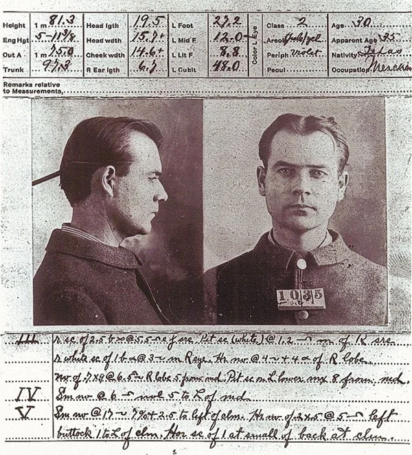 A black and white mugshot of a man with short hair, wearing a dark coat. The image shows two views: a profile view on the left and a front view on the right. The man has a serious expression. The top of the image contains handwritten measurements, and the bottom contains handwritten notes.