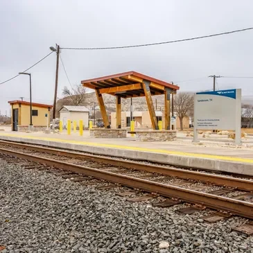 Empty train station platform with a covered waiting area, signboard, and train tracks in a small town.