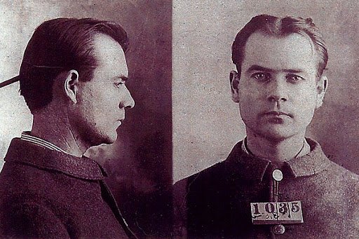 Black and white mugshot of a young man with short hair, wearing a high-collared uniform, facing forward with a serious expression, and a numbered placard reading '10385'.