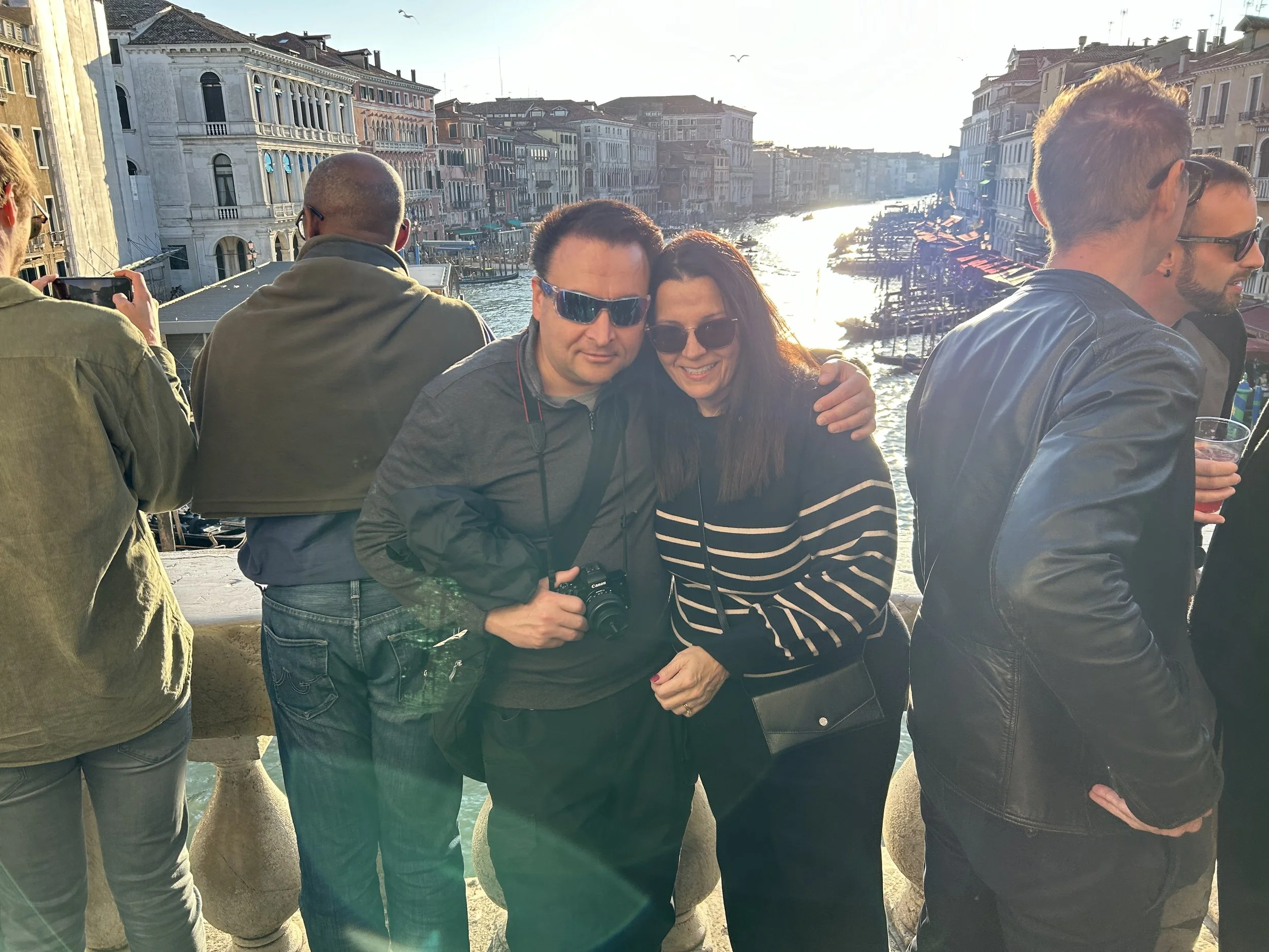 TRICRAFT CEO husband and wife Angela Renne Cross  overlooking a canal with boats, during sunset in Venice, Italy.