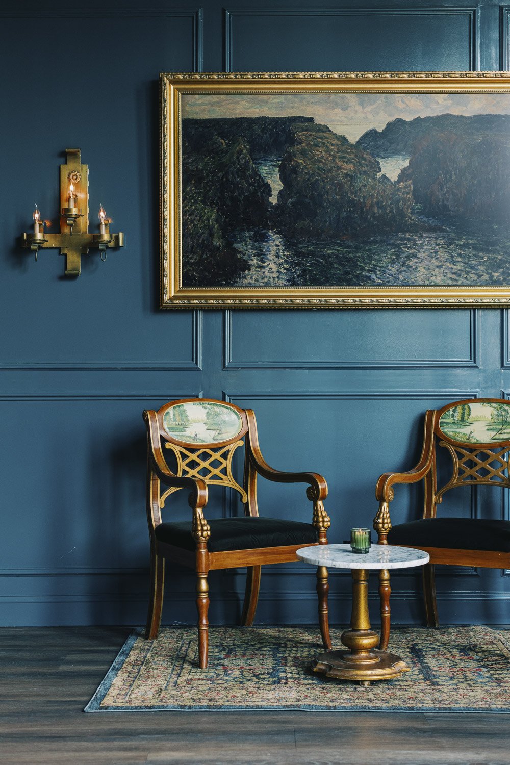 Vintage dining chairs and picture frame against a paneled wall with decorative mouling 