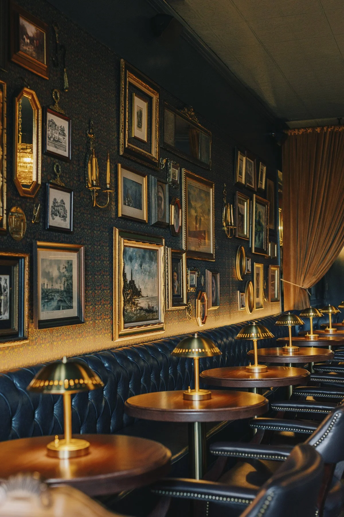 Gallery wall above a Chesterfield-style banquette with dining tables and table lamps