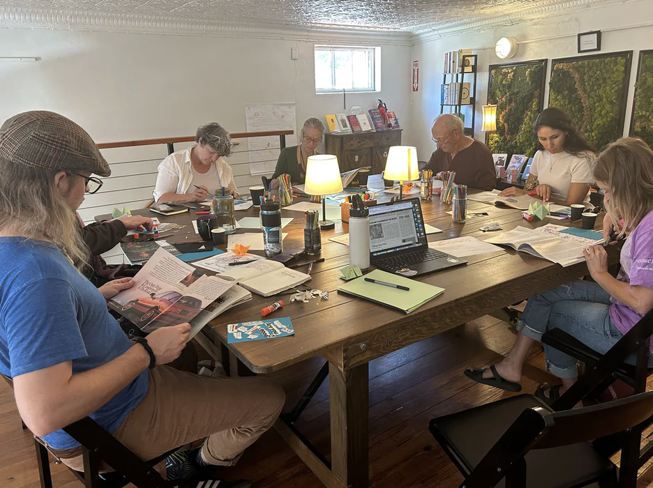 A group of people in a workshop sit around a large table working on art projects.