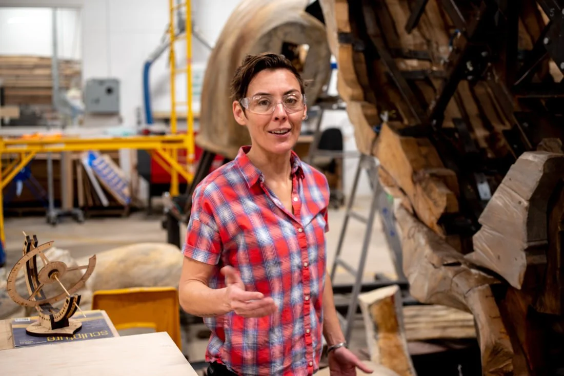 Sara Sanders, wearing a red plaid shirt and safety glasses, stands in the UNC Asheville STEAM studio.