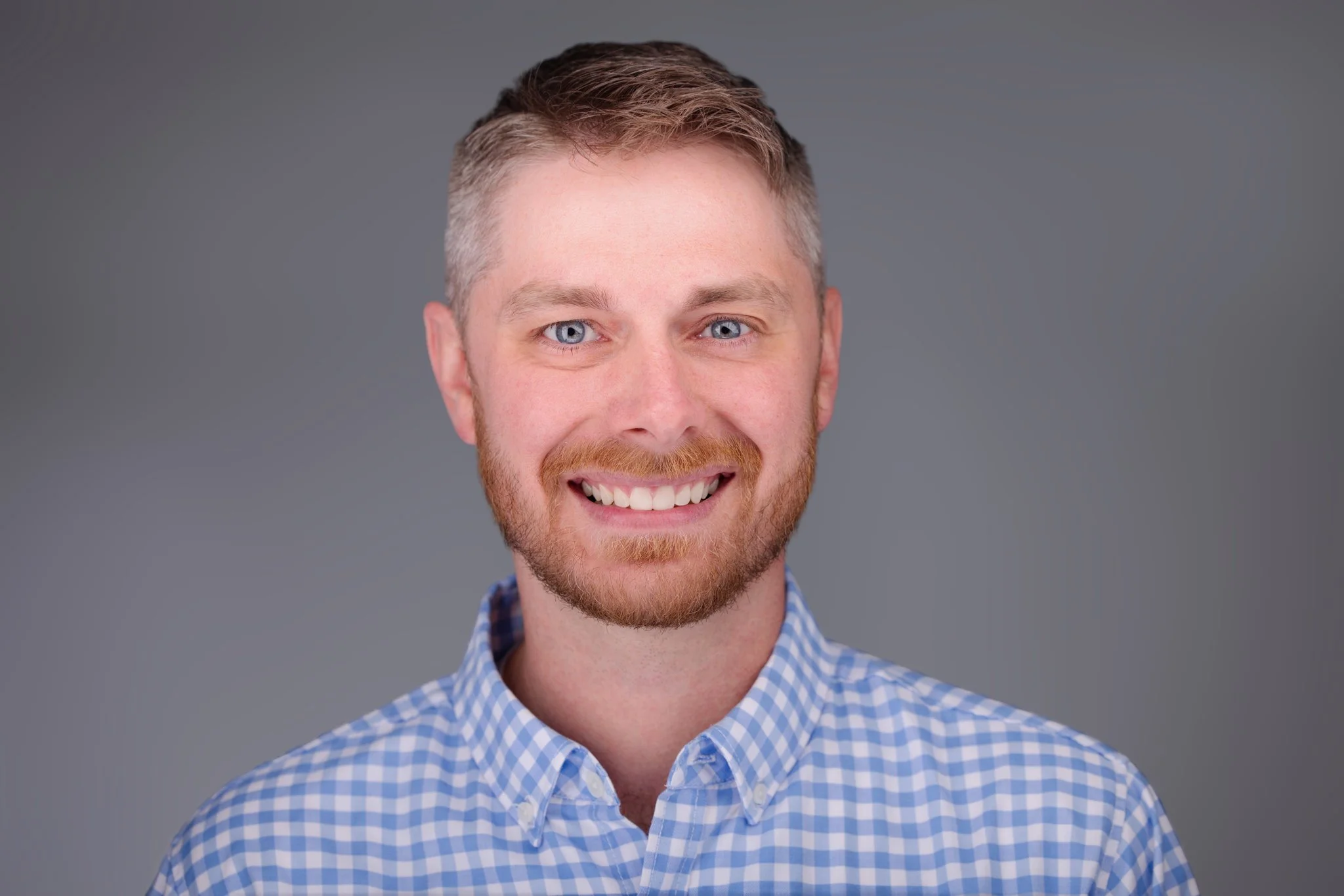 A man with blue checker shirt on with a solid gray background