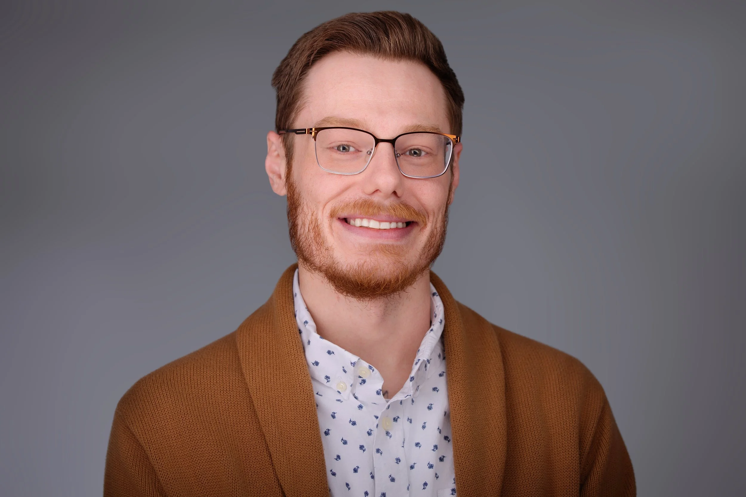 Professional headshots of a man with brown sweater and glasses 