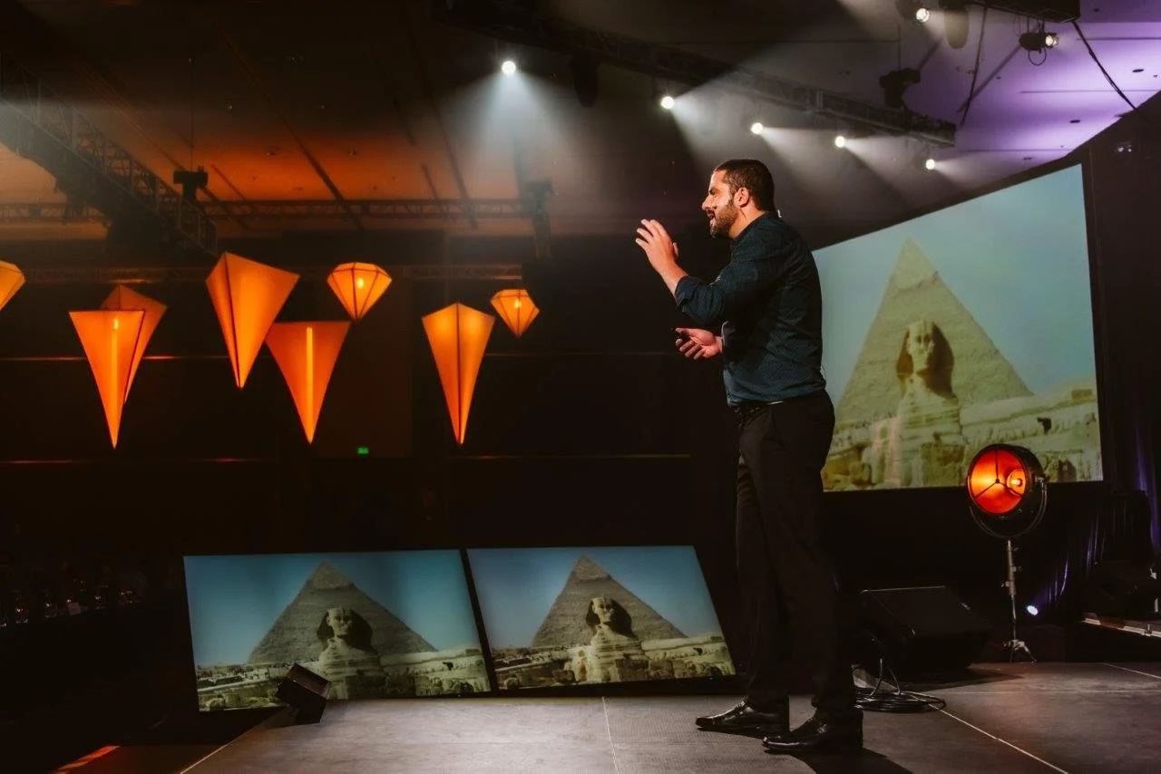 Grupo en un escenario de teatro con iluminación azul, con una persona hablando y varias sentadas en sillas.