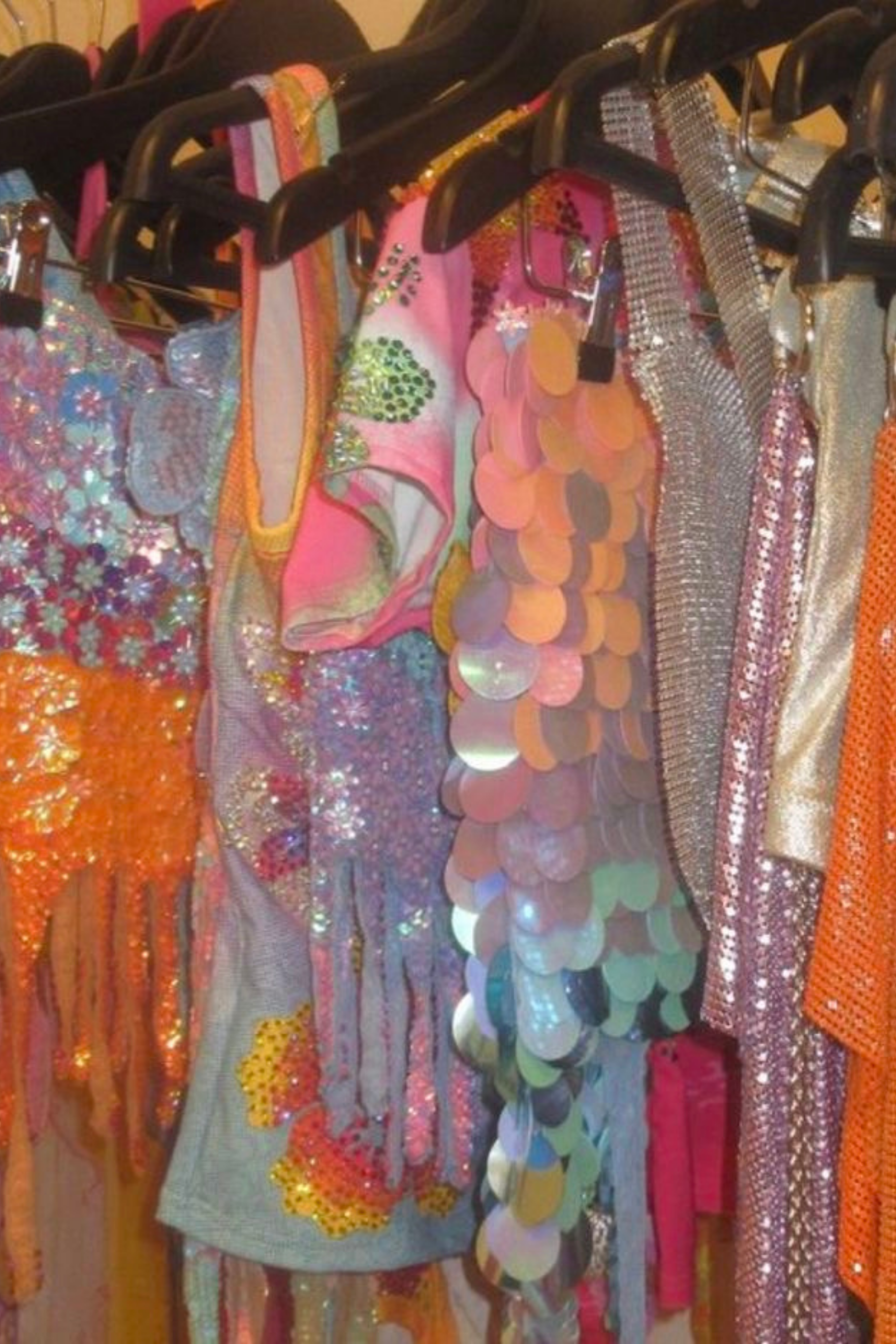 Colorful fabric and sequin garments hanging on black hangers on a rack.