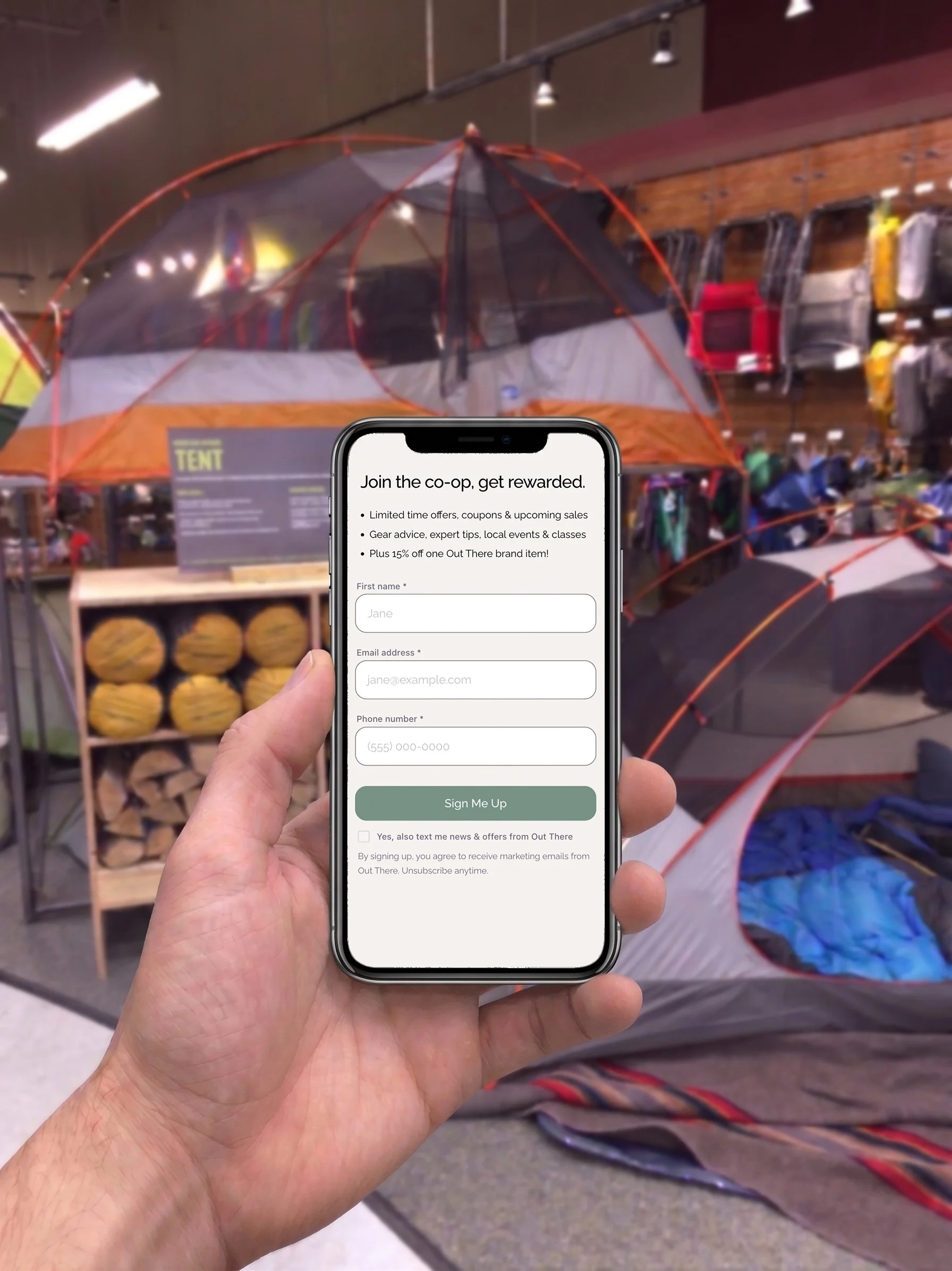 A person holding a smartphone displaying a sign-up form for a co-op membership with the store in the background.