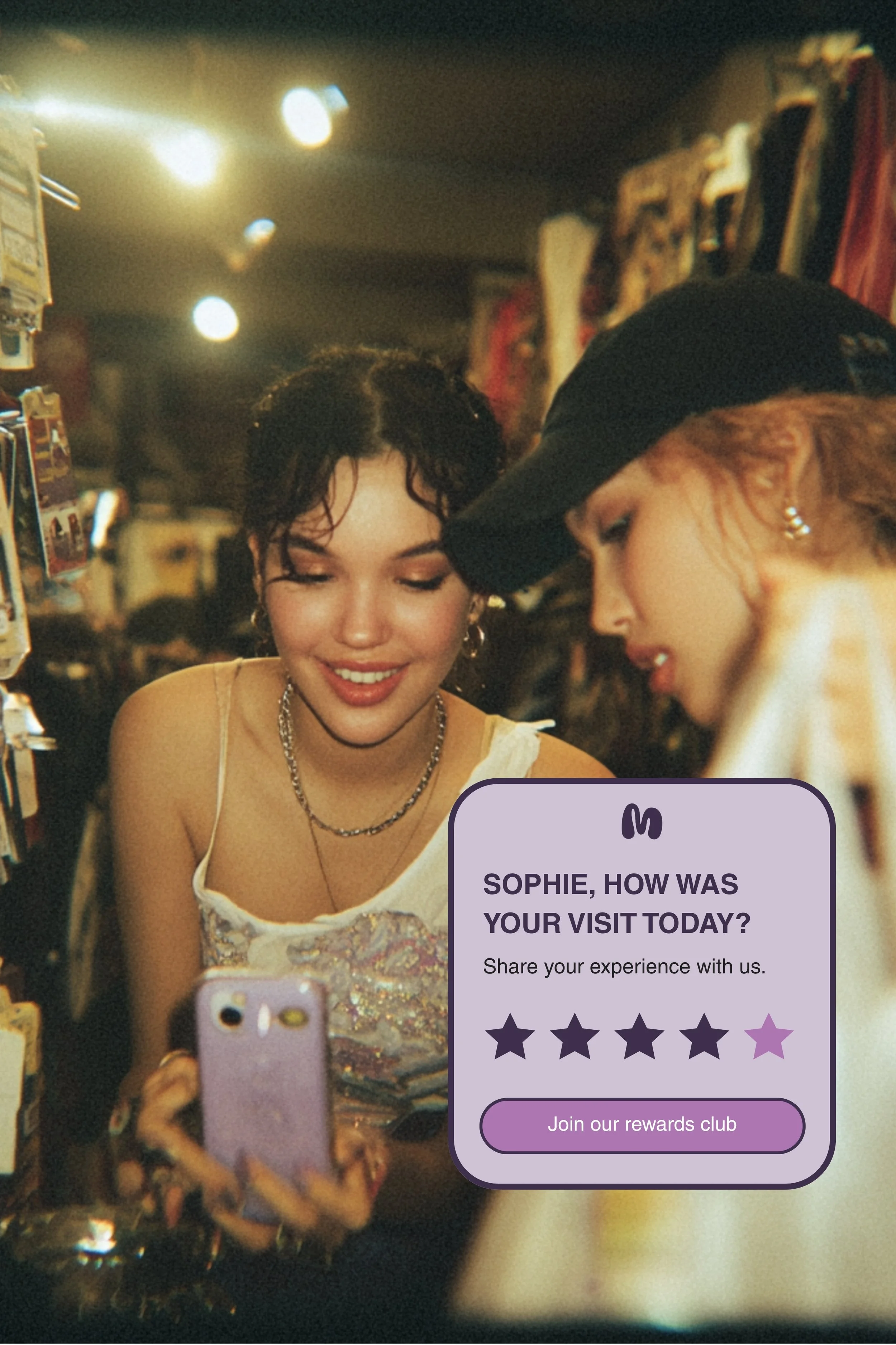 Two women in a store looking at their phones. One woman has dark hair with earrings and is wearing a sleeveless top. The other woman has red hair, a cap, and earrings. There are packages on shelves around them, and a speech bubble overlay at the bottom with a review asking 'Sophie, how was your visit today?'