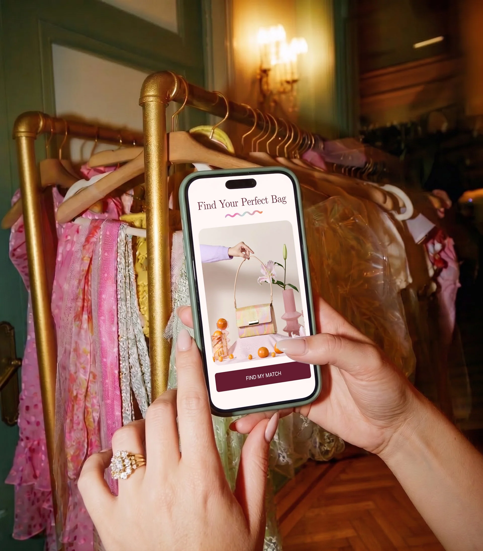 Person holding a smartphone with an app called "Find Your Perfect Bag" open, showing various handbag styles, in front of a clothing rack with dresses on hangers, in a room with wooden flooring and a warm light fixture on the wall.