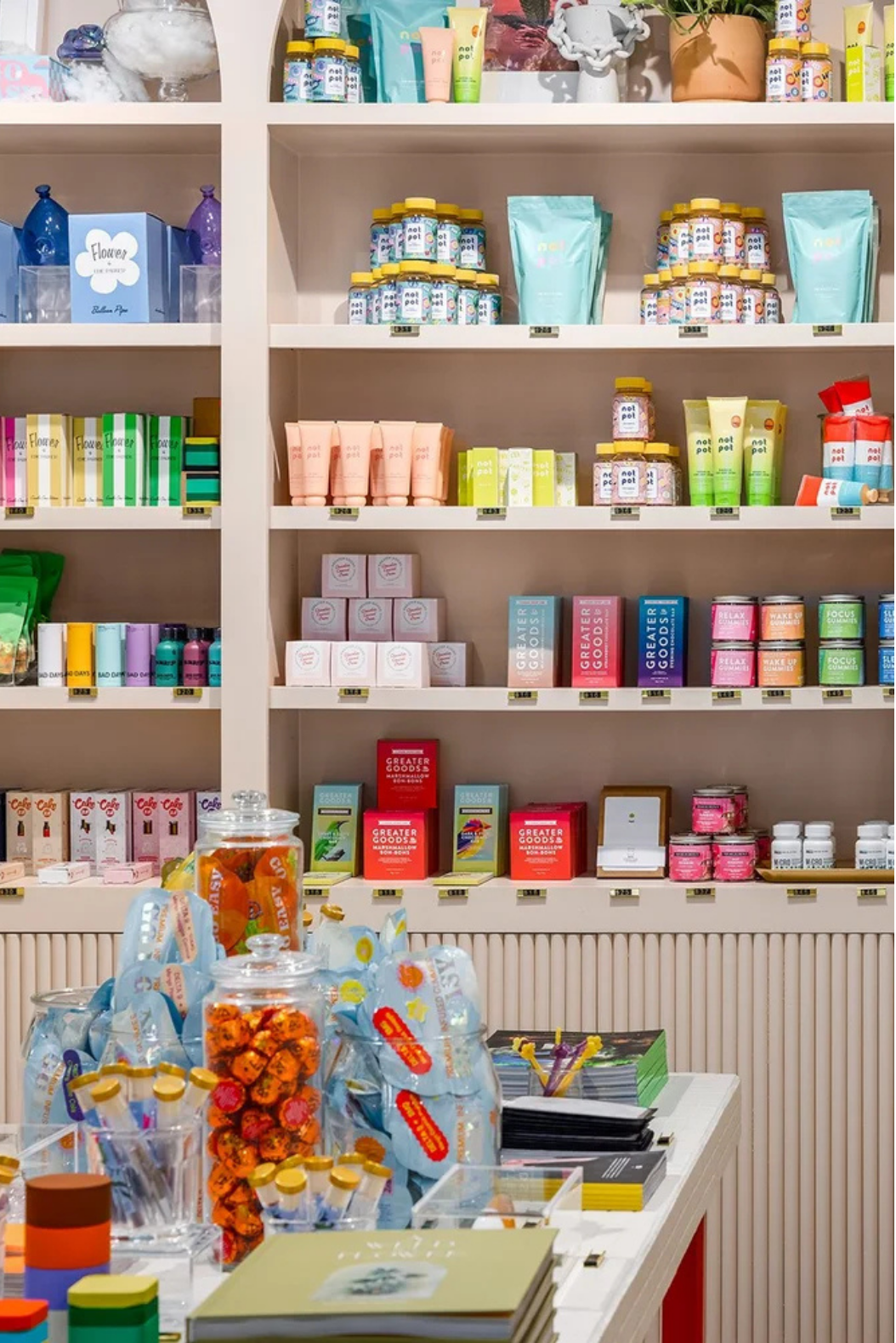 Shelves stocked with colorful health and wellness products, including bottles, boxes, and bags, with a display of candies and small novelty items on a table in the foreground.