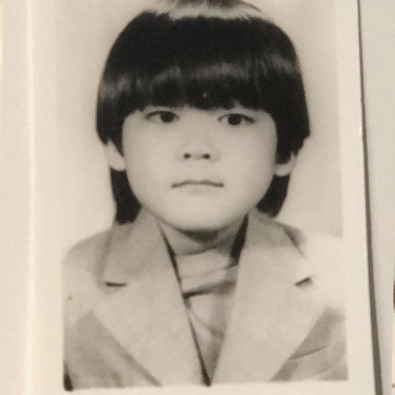 Black and white portrait of a young boy with straight dark hair, wearing a collared jacket and a turtleneck shirt.