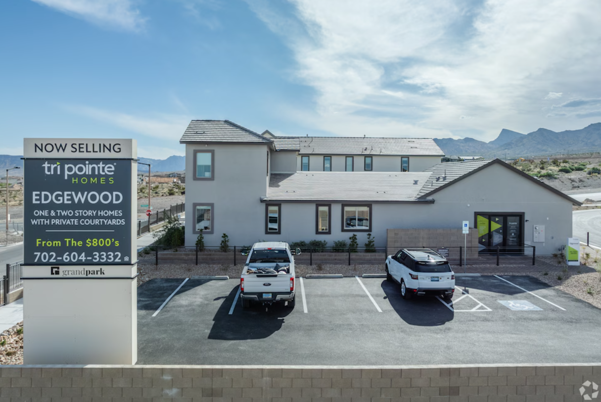 Parking lot in front of a two-story building with a sign and a mountainous landscape in the background.