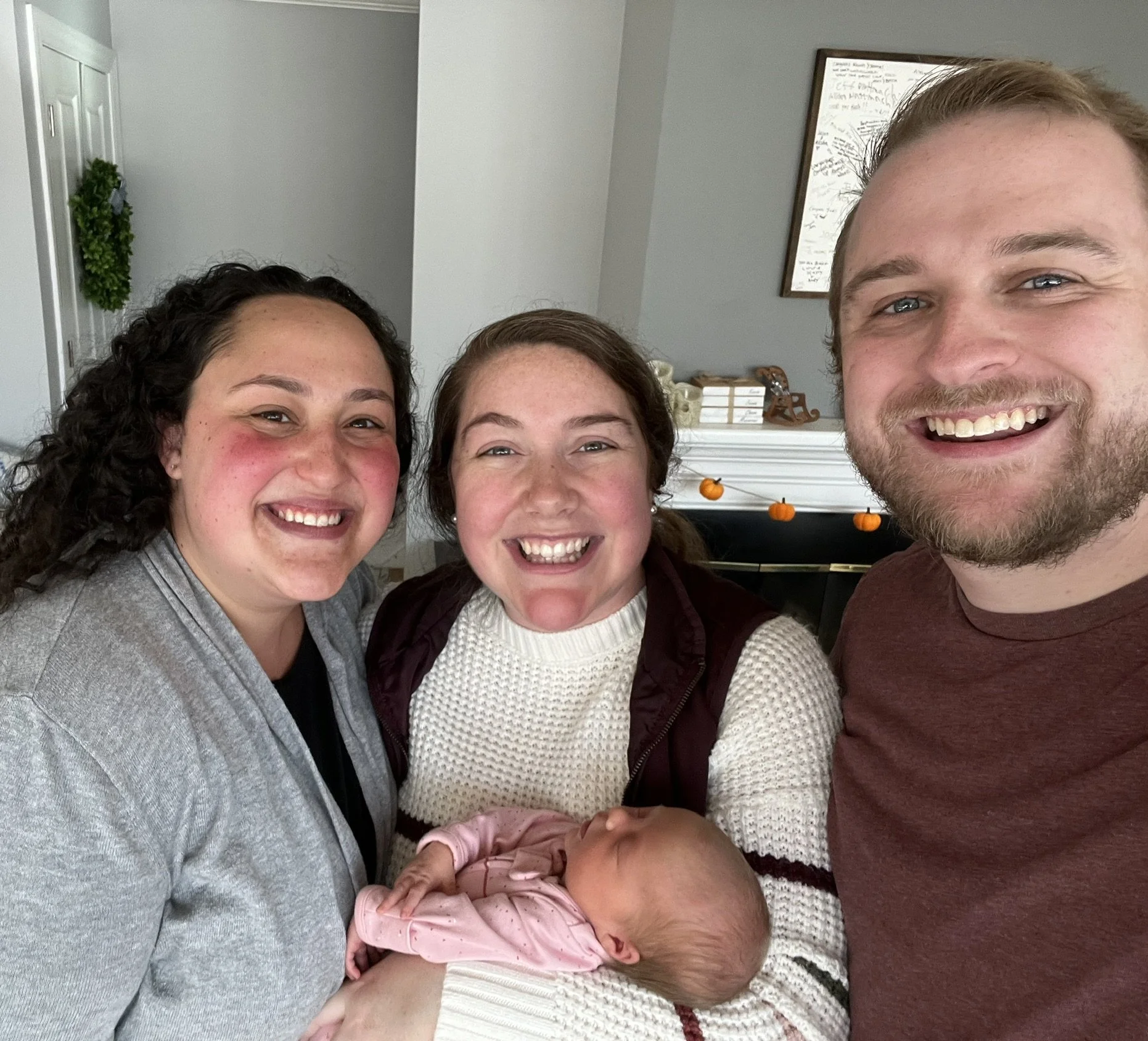 A newborn baby lying on a hospital bed, holding an adult's finger, with an adult nearby wearing a yellow tie-dye shirt featuring a tiger logo.