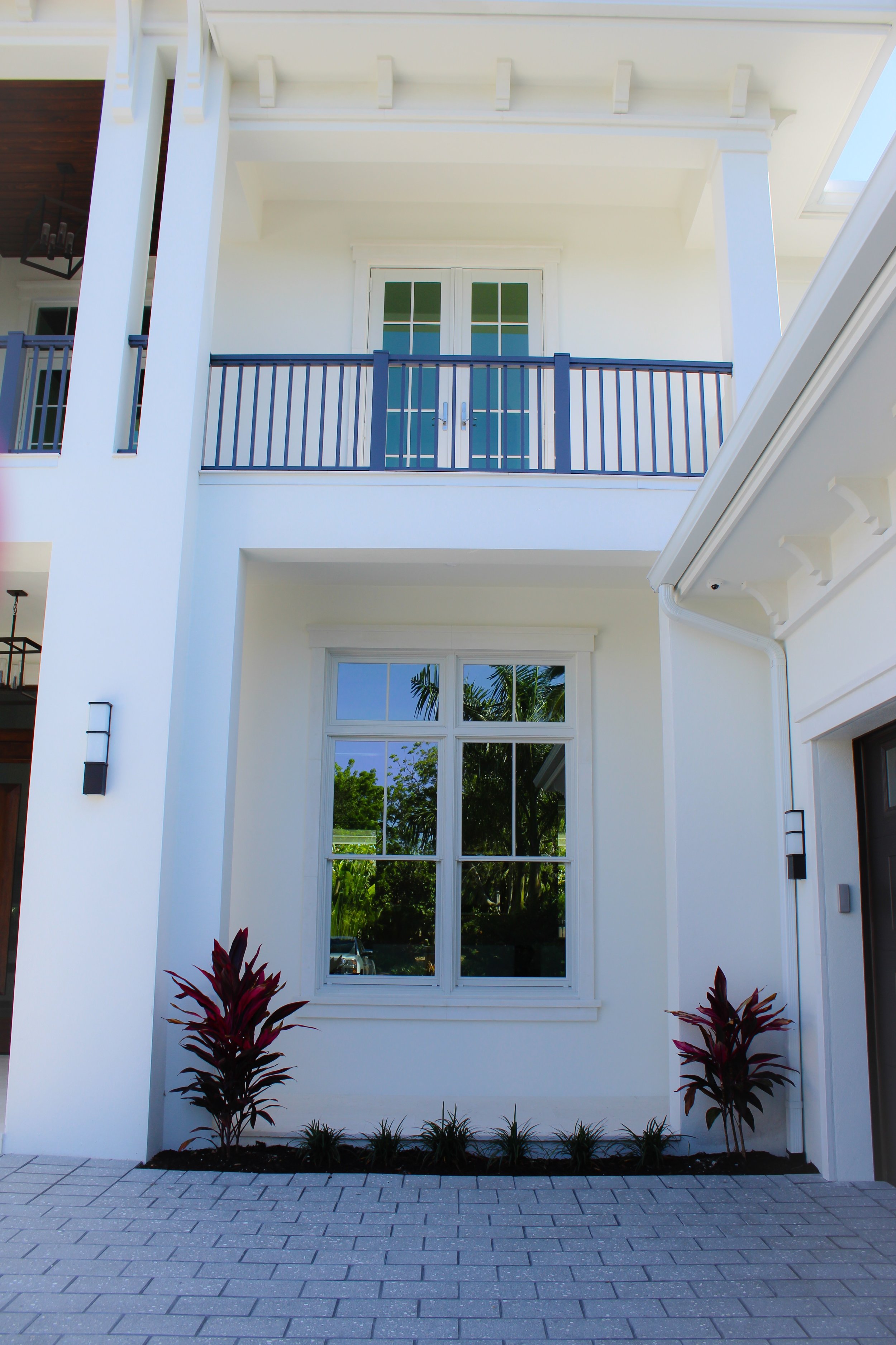 White house exterior with large window and a balcony with a double door above. 