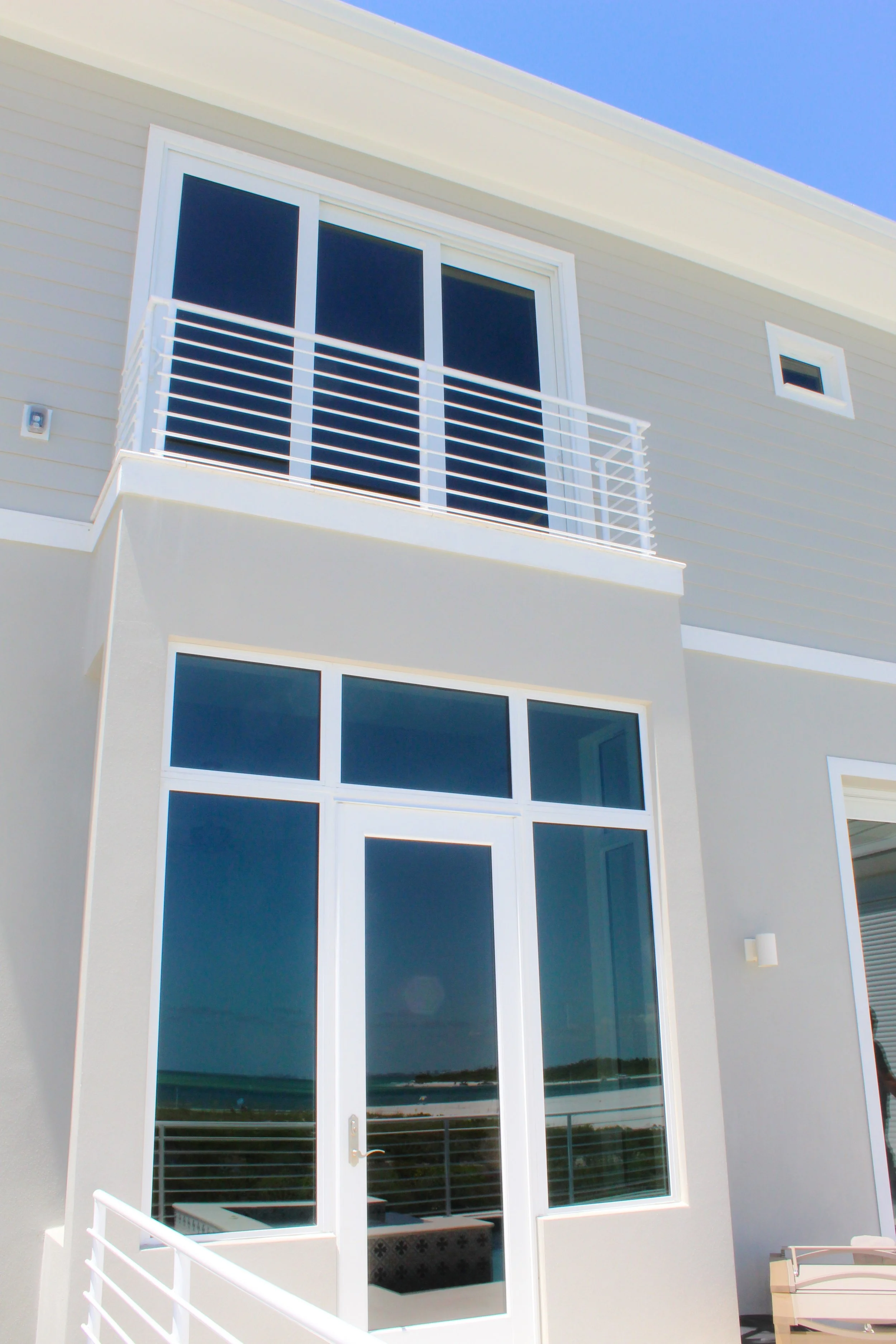 Exterior view of a modern beach house with a sliding glass door on a small balcony above a system of large windows connected to a single exterior door.