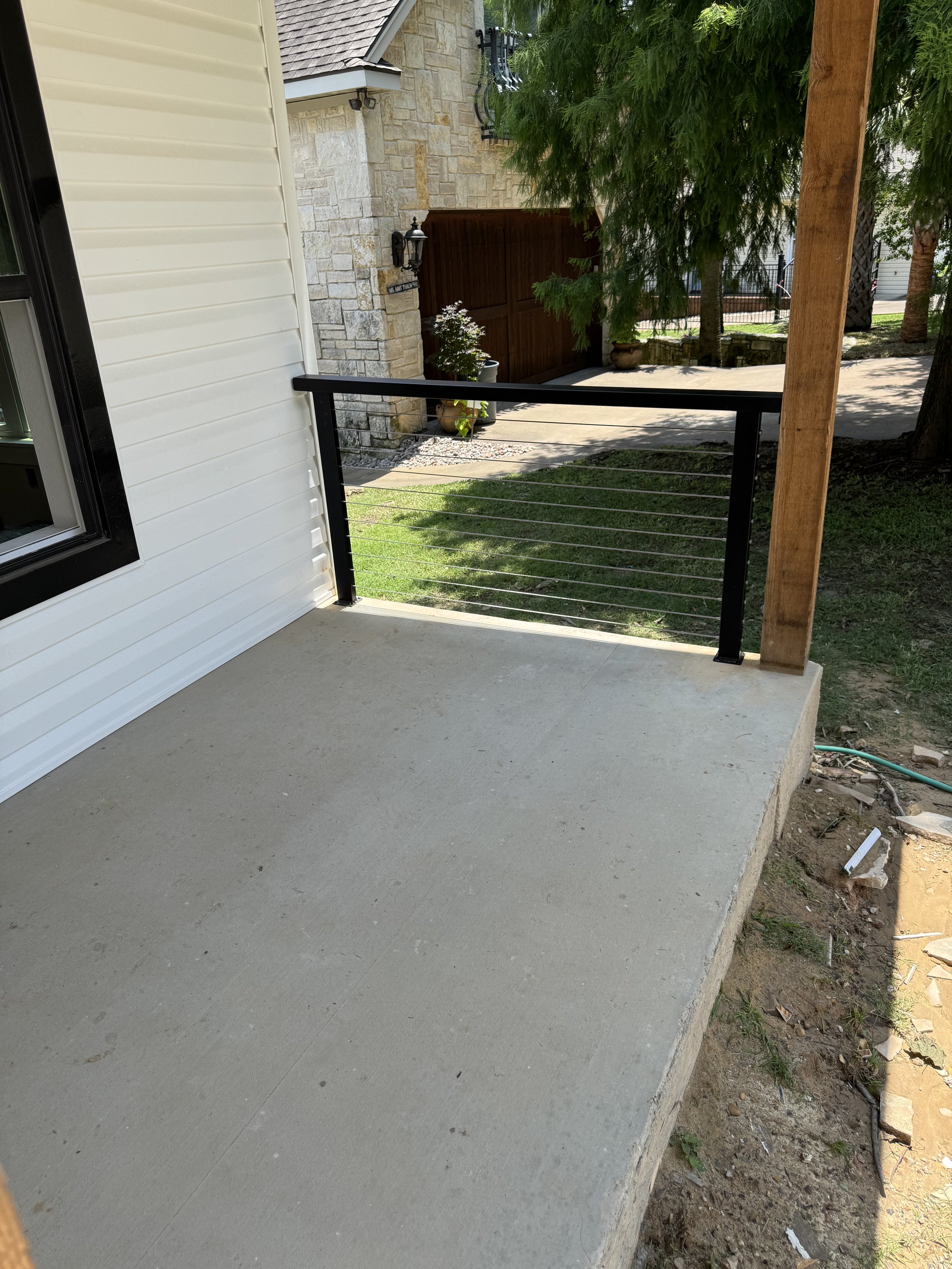 View of a new concrete patio with a black metal and cable railing. 