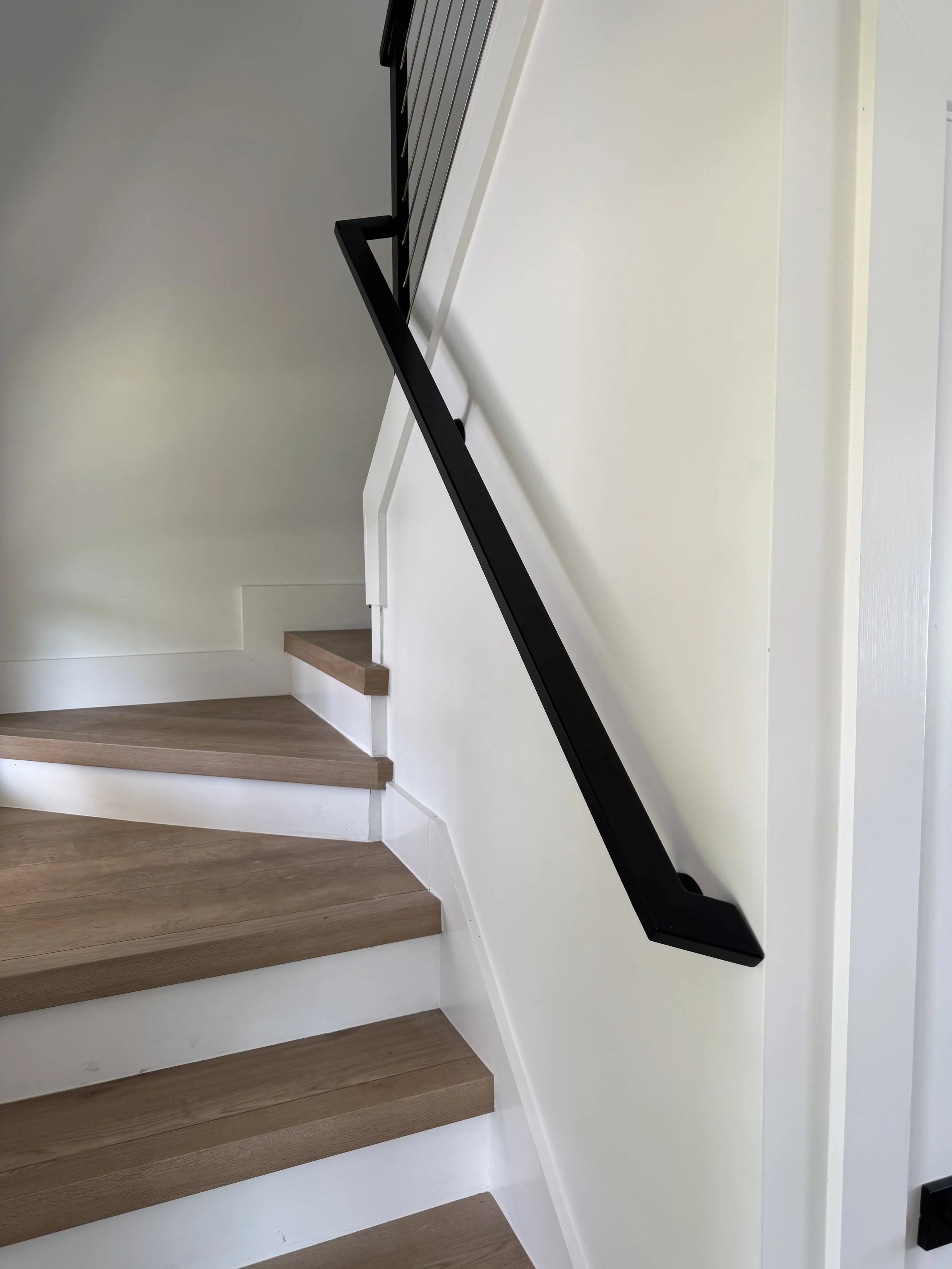Close-up view of a modern staircase with wooden steps and a black metal handrail. 