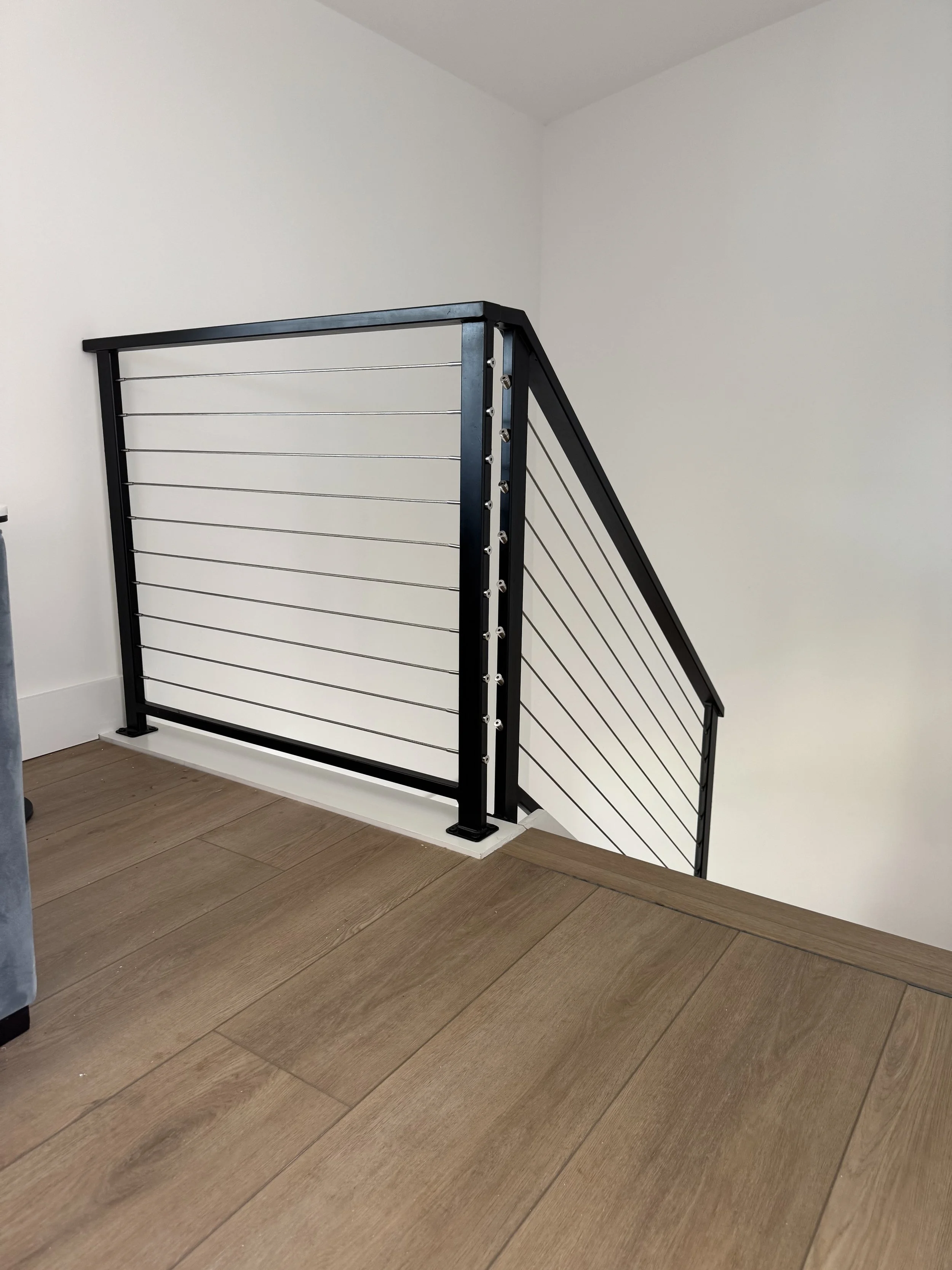 Interior staircase with black metal railing and cables. 