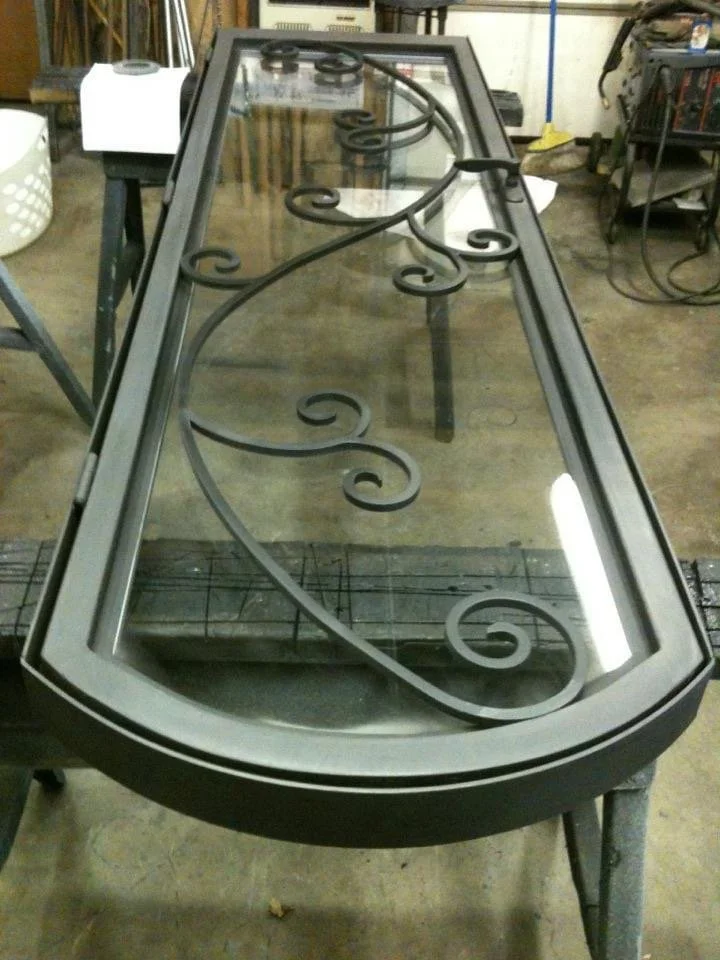 A decorative glass and metal table with ornate black iron scrollwork in a workshop setting.