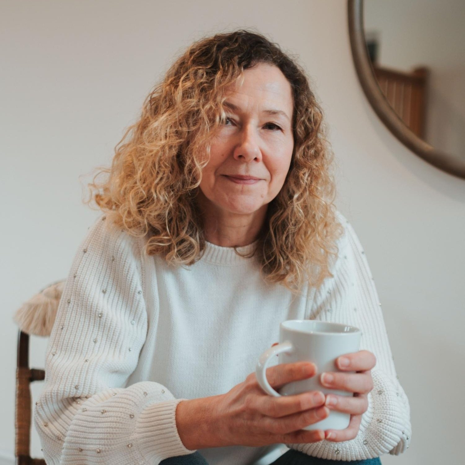 Your Life Hypnotherapy Services - Person with curly hair holding a white mug in a cozy setting, wearing a light sweater.