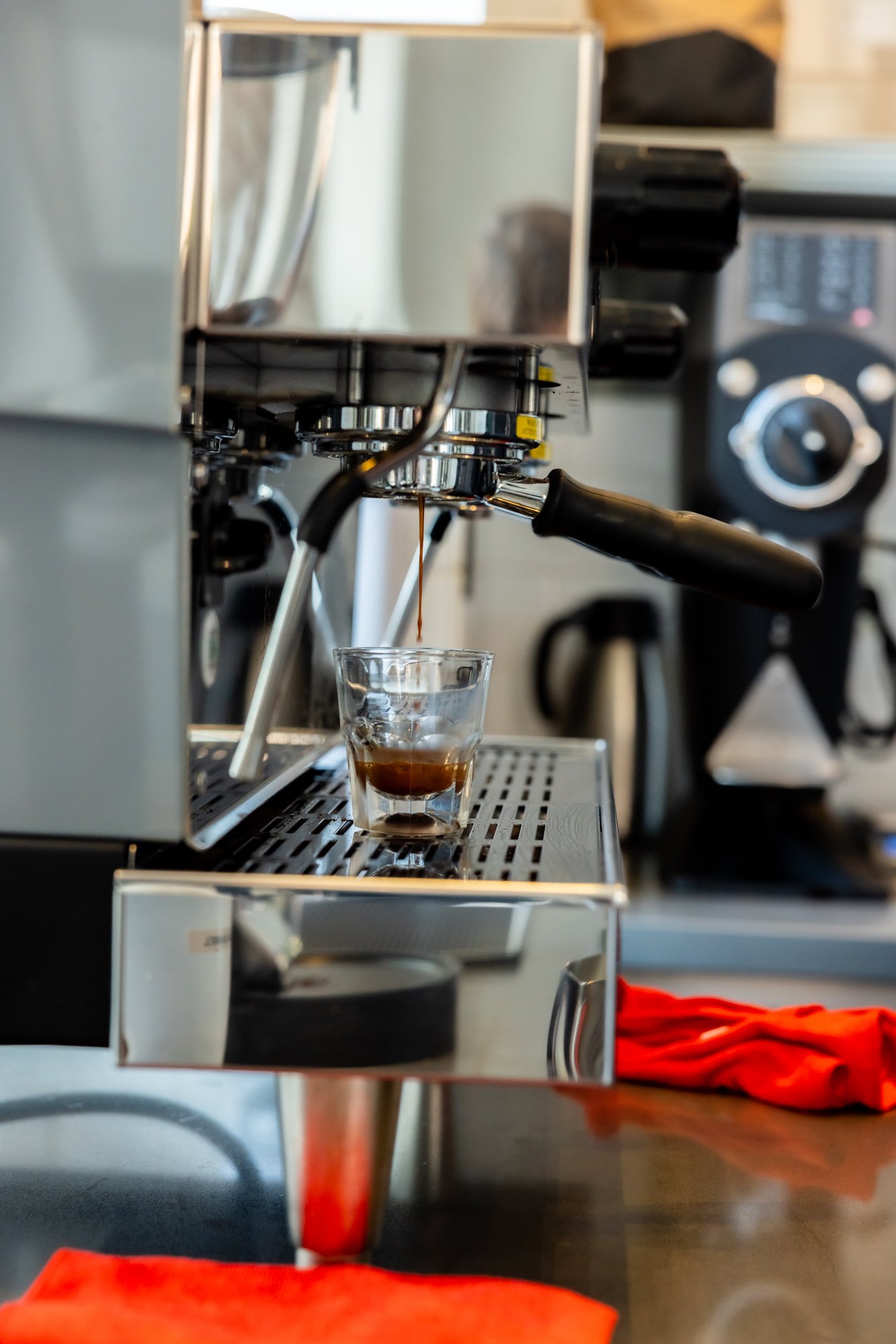 Close-up of a coffee espresso machine pouring espresso into a glass cup, with a background of kitchen appliances.