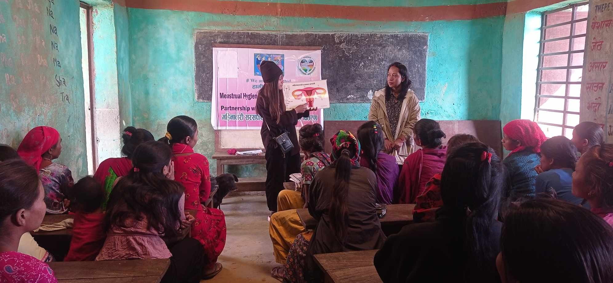 Group of Nepalese women attending a menstrual hygiene workshop with a Days for Girls presenter holding an educational poster in a classroom setting. With Eternal Hope International